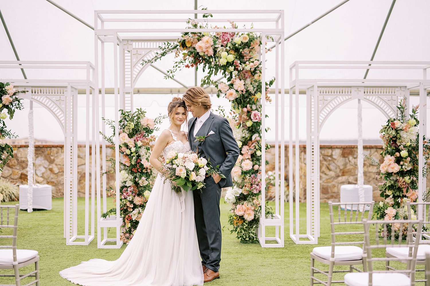 bride and groom pose by floral arbor at Bella Collina