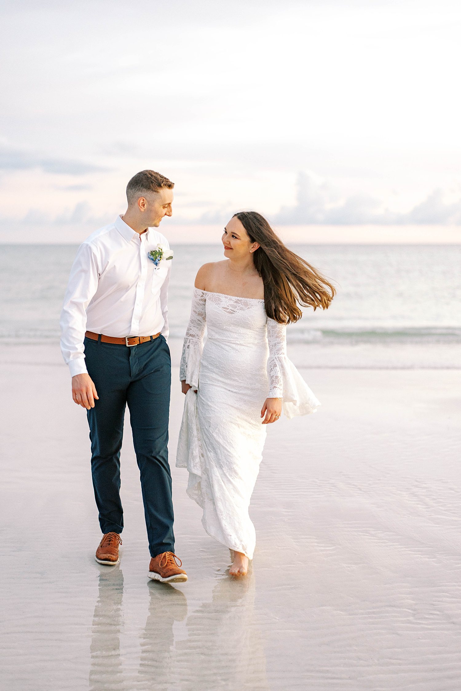 bride and groom hold hands walking on beach