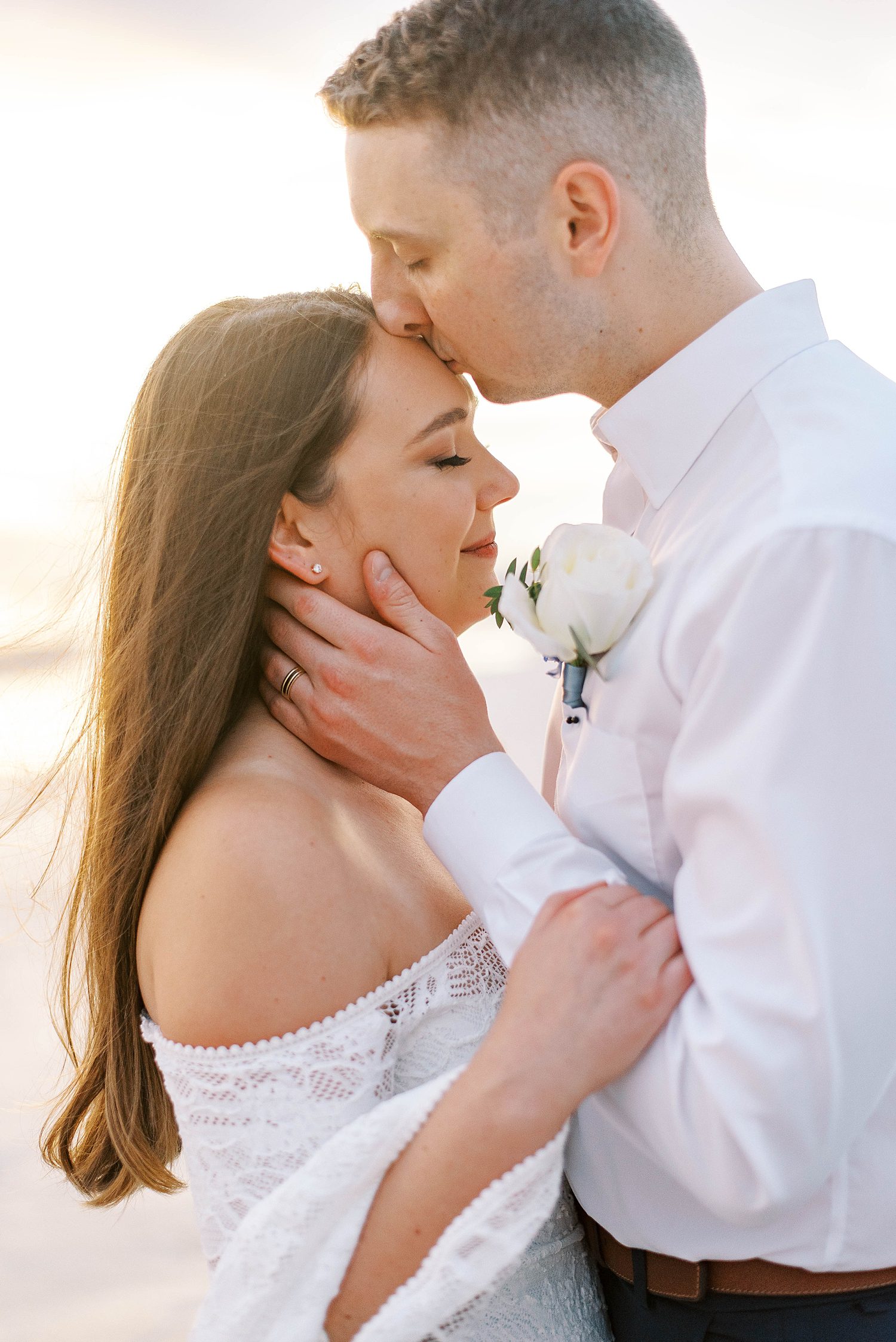 groom kisses bride's forehead on beach in Florida 