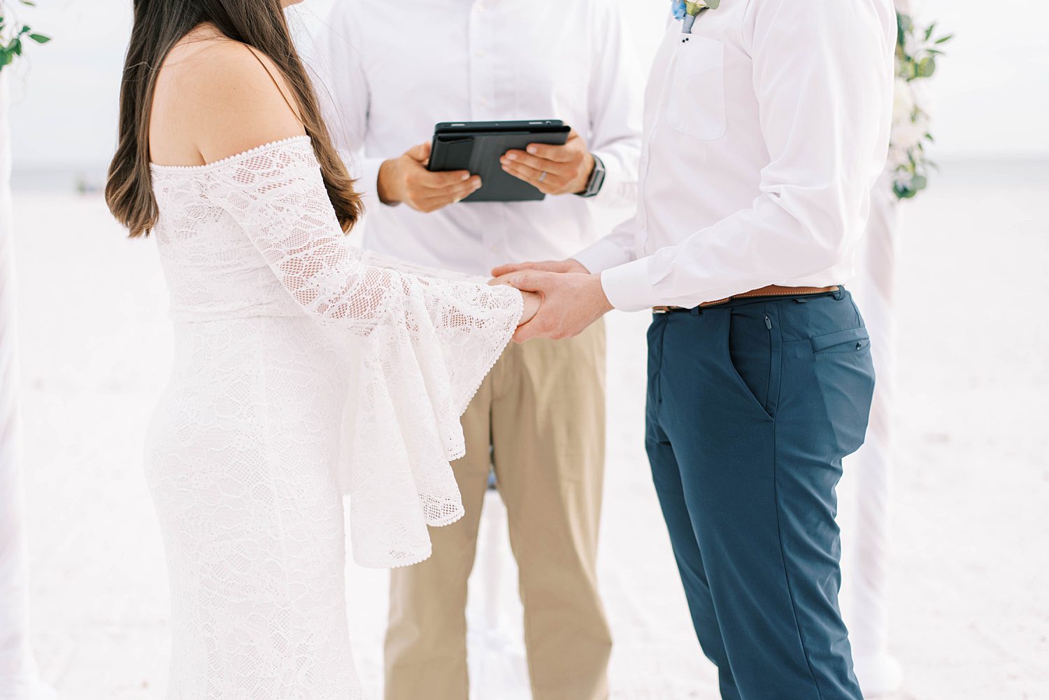 bride and groom hold hands standing on beach