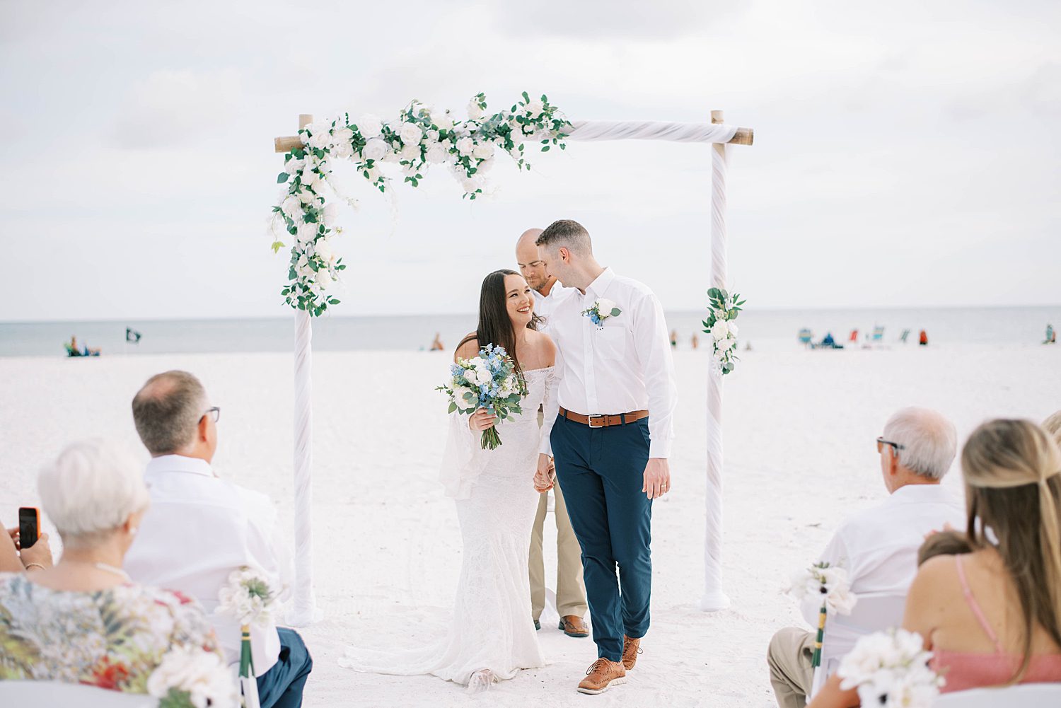 bride and groom kiss under floral arbor on Lido Key Beach