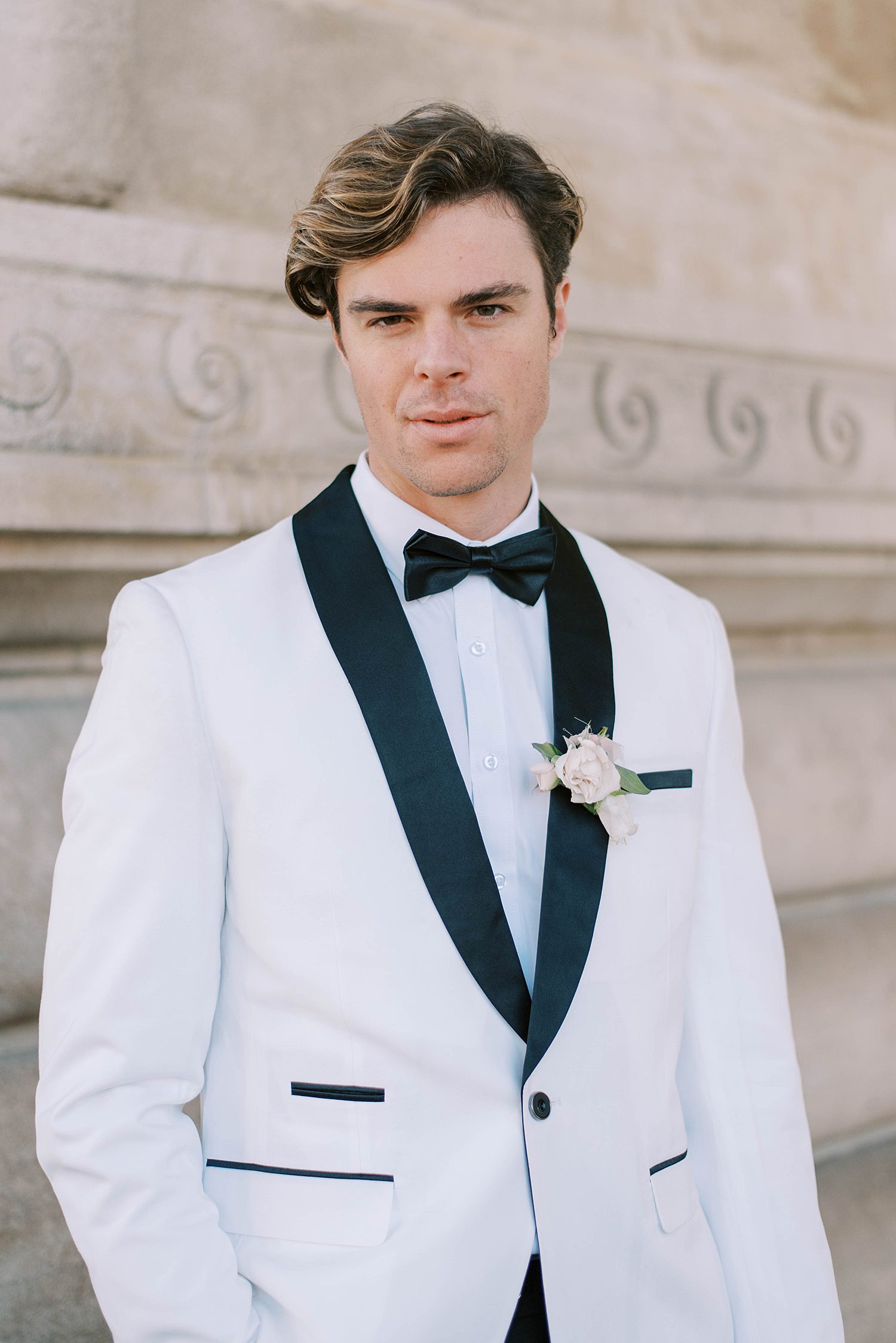 groom stands in white tux jacket in Paris