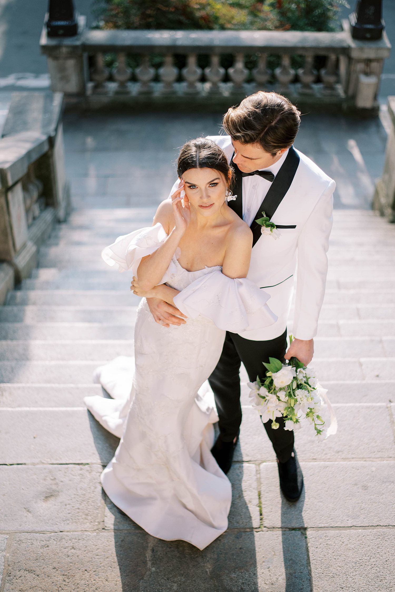 groom in white tux jacket holds bride on walkway in Paris
