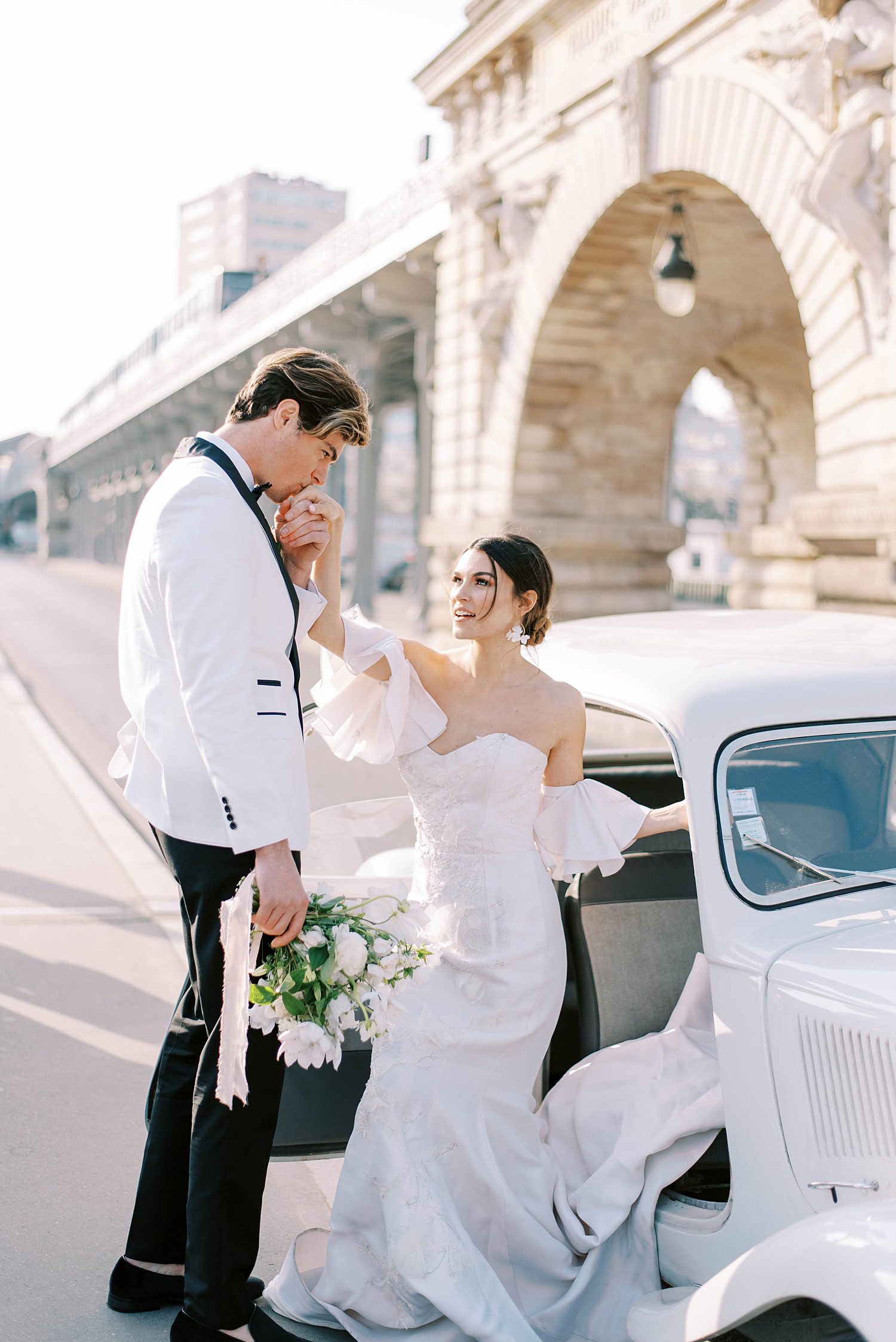 groom helps bride out of car and kisses her hand in Paris