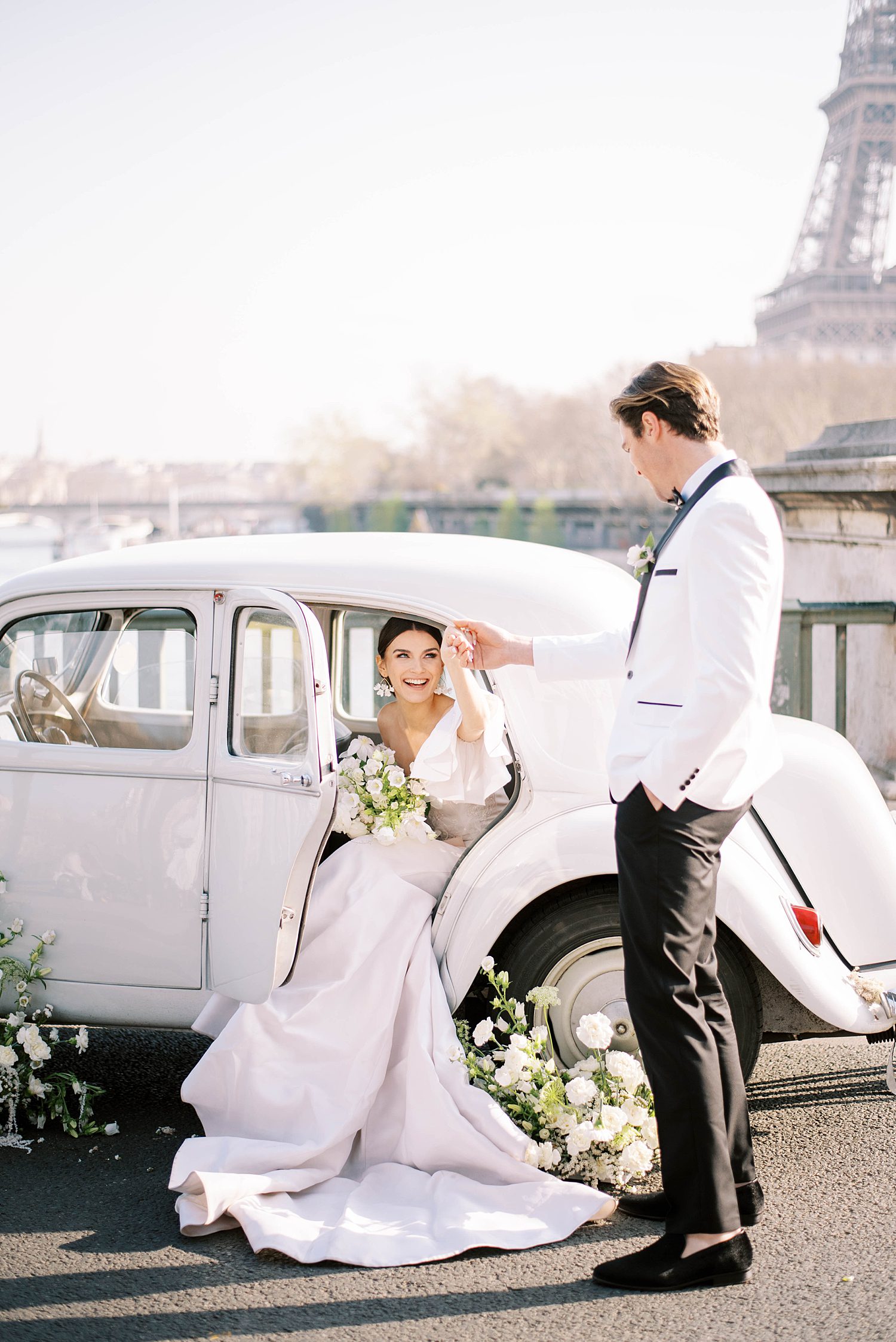 groom in white tux jacket helps bride out of classic car during Paris elopement 