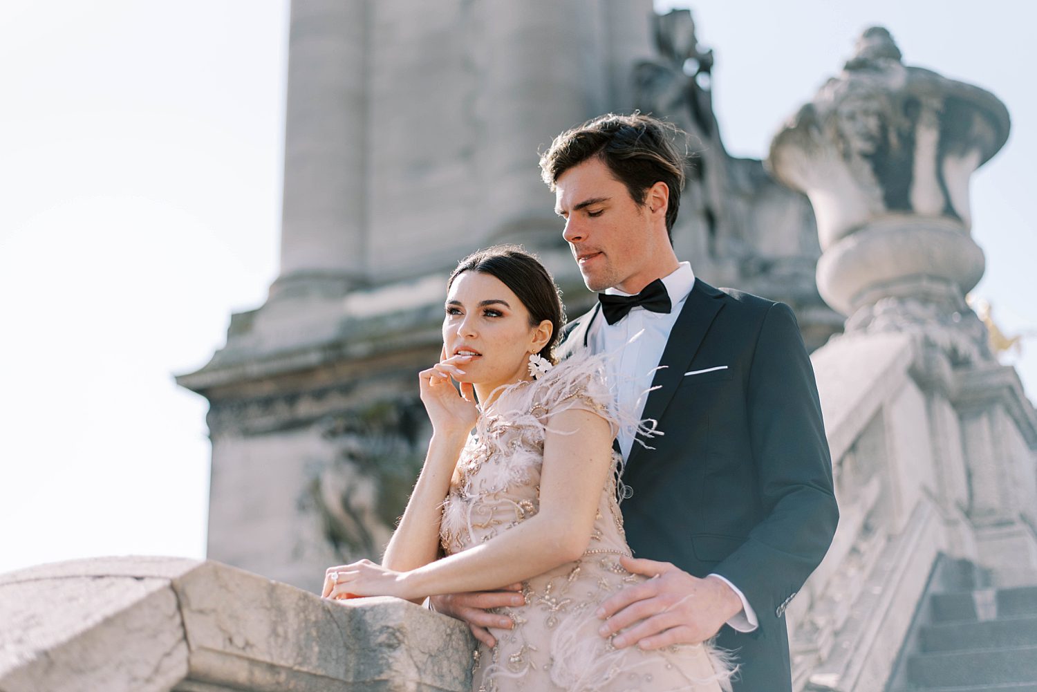 groom stands by bride in blush gown on Paris steps