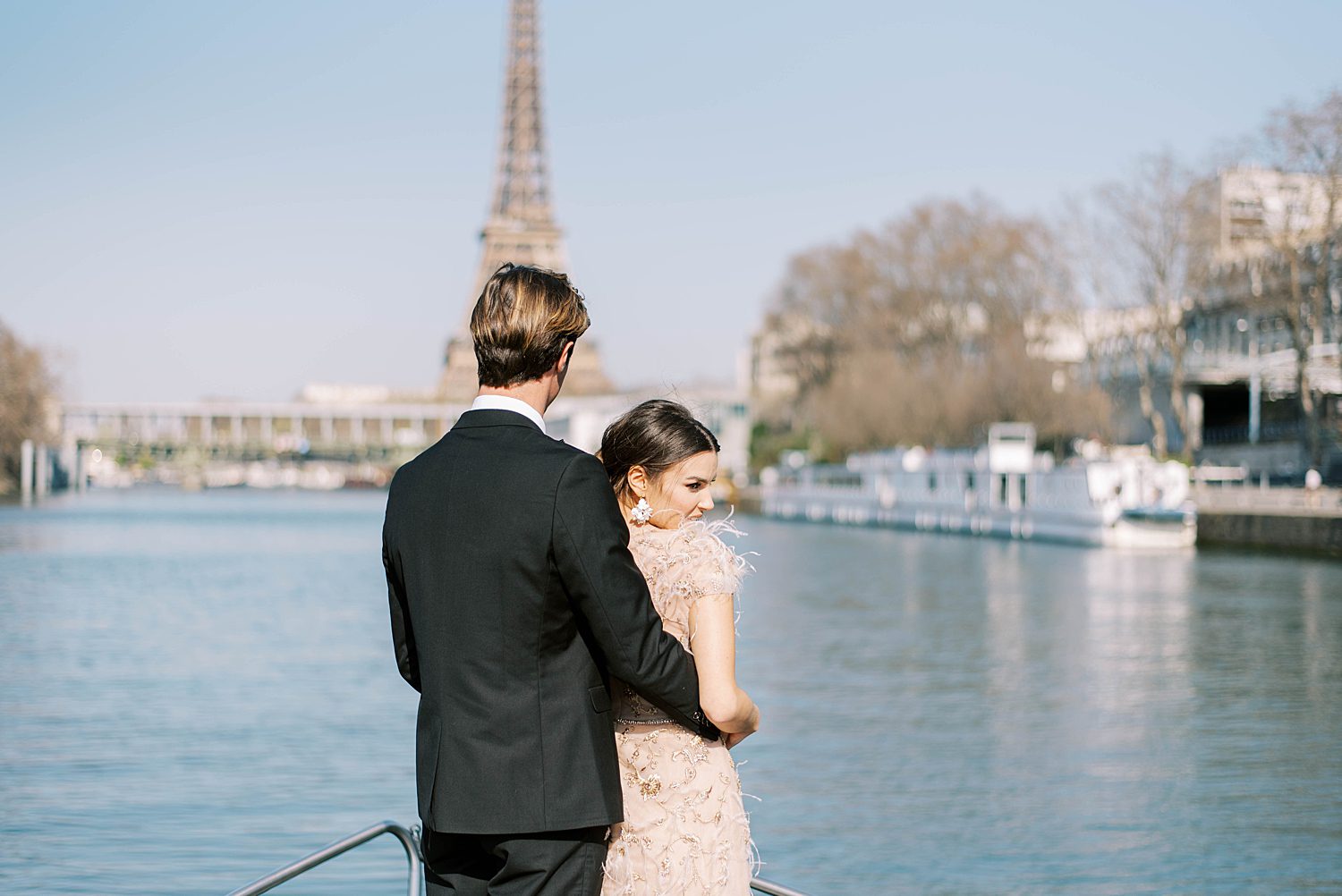 groom holds bride on front of boat looking at Paris