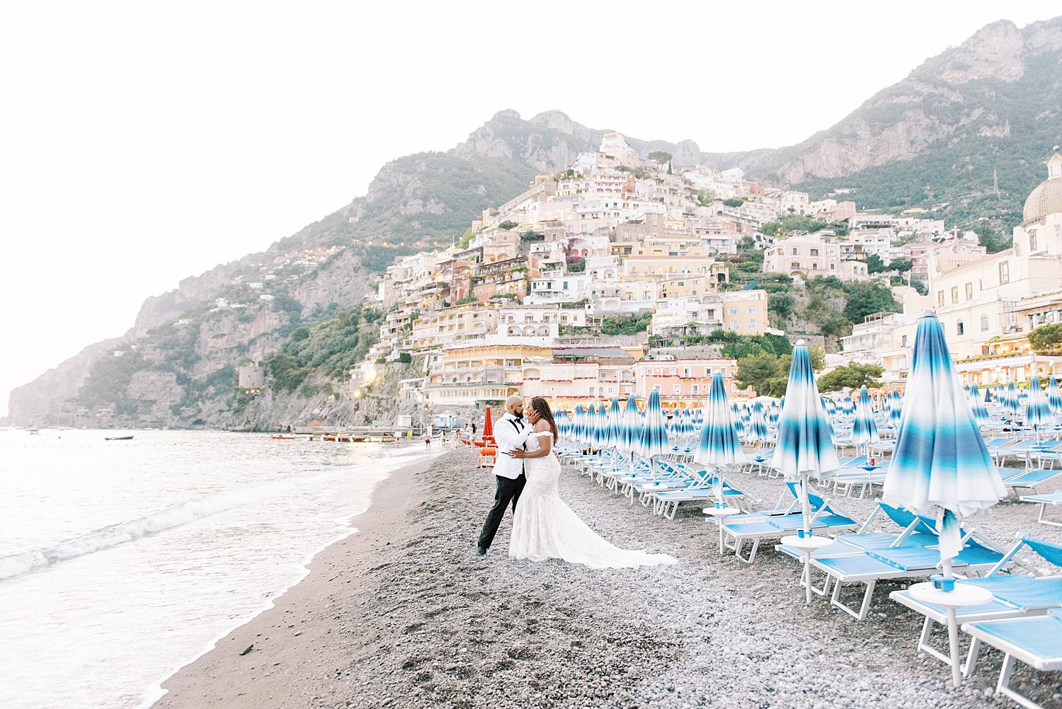 newlywed pose by blue and white umbrellas on Positano during Amalfi Coast elopement