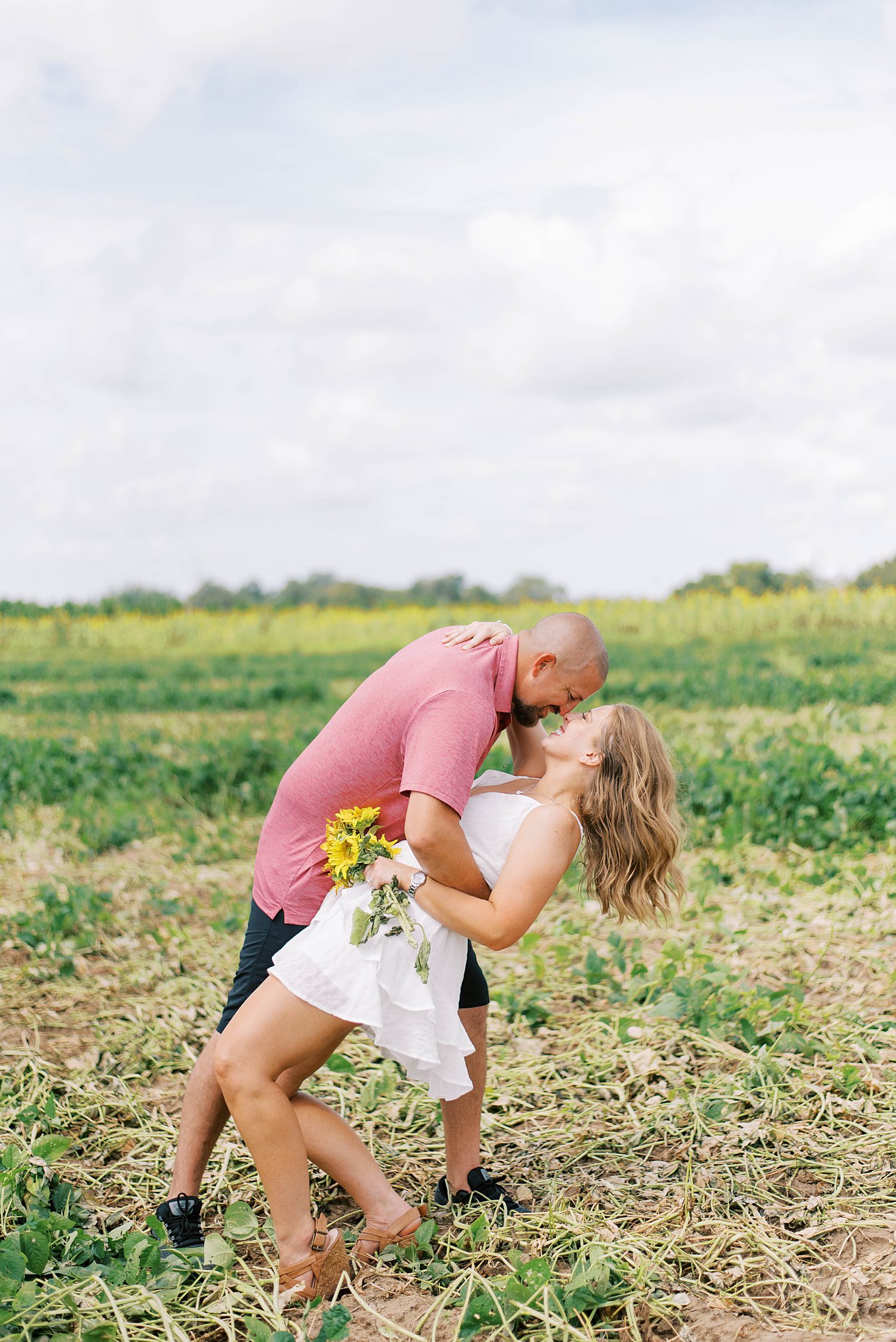 groom dips bride kissing her during Tampa FL sunflower field engagement session 
