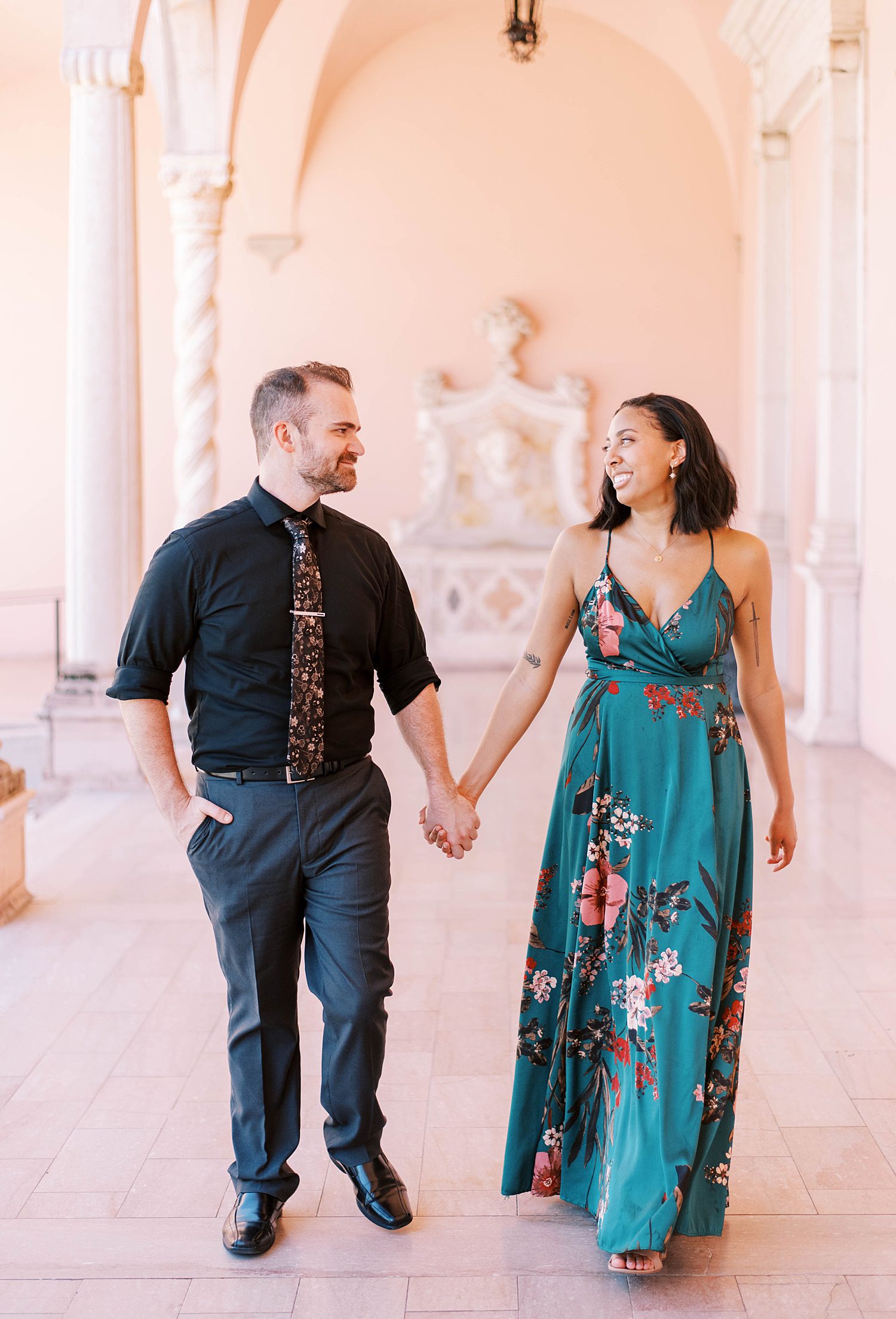engaged couple holds hands walking down pink hallway during the Ringling Museum engagement session
