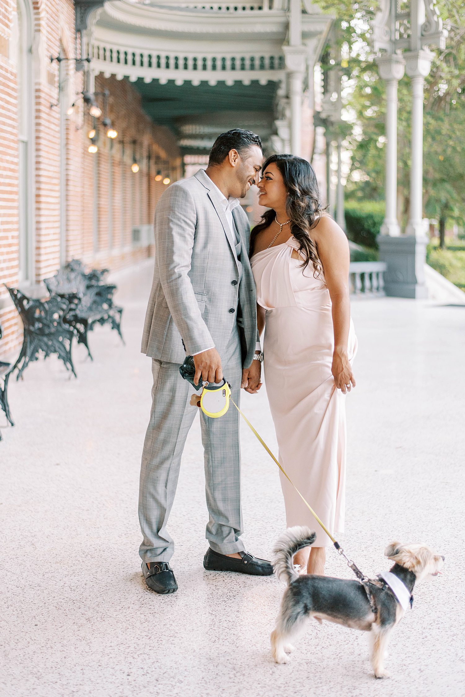 engaged couple leans together during University of Tampa photos with dog in front of them