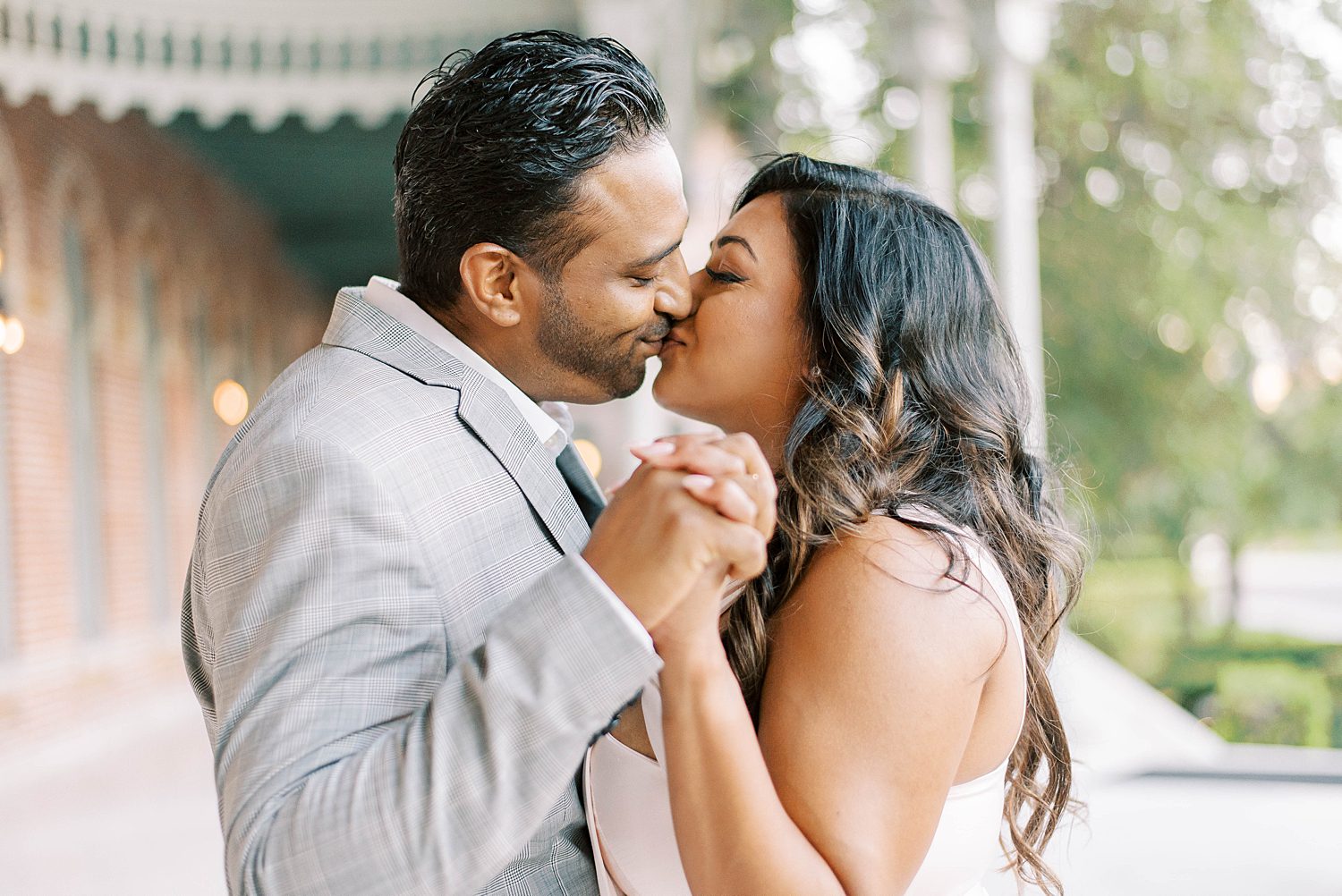 engaged couple holds hands leaning to kiss