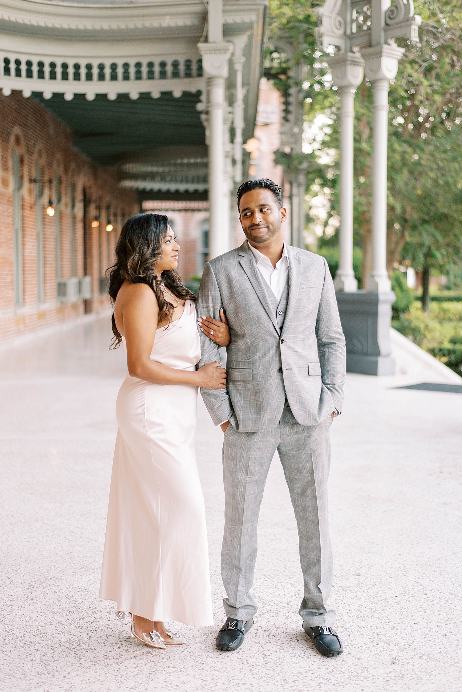 woman holds fiancee's arm looking at him in grey suit