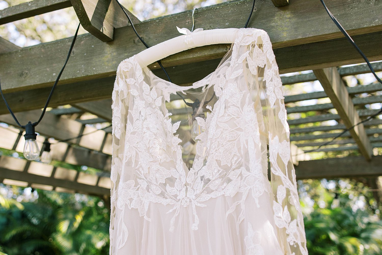 lace wedding dress hangs on wooden arbor at Events Under the Oaks