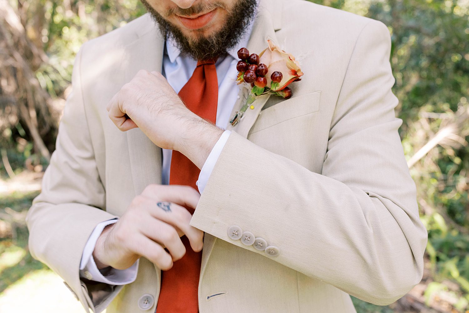 groom adjusts sleeve of tan suit during portraits at Events Under the Oaks