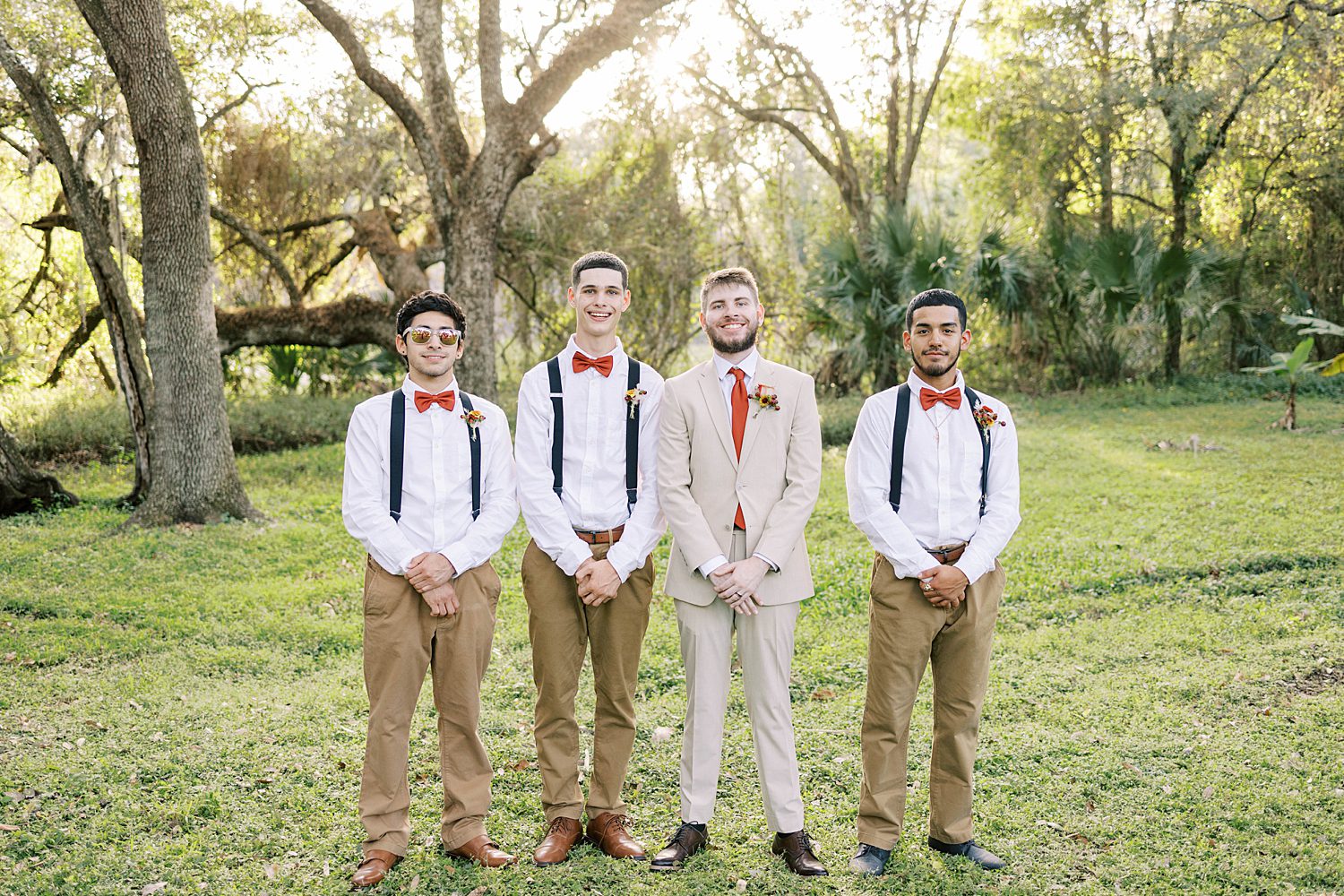 groom poses with groomsman in suspenders and orange ties