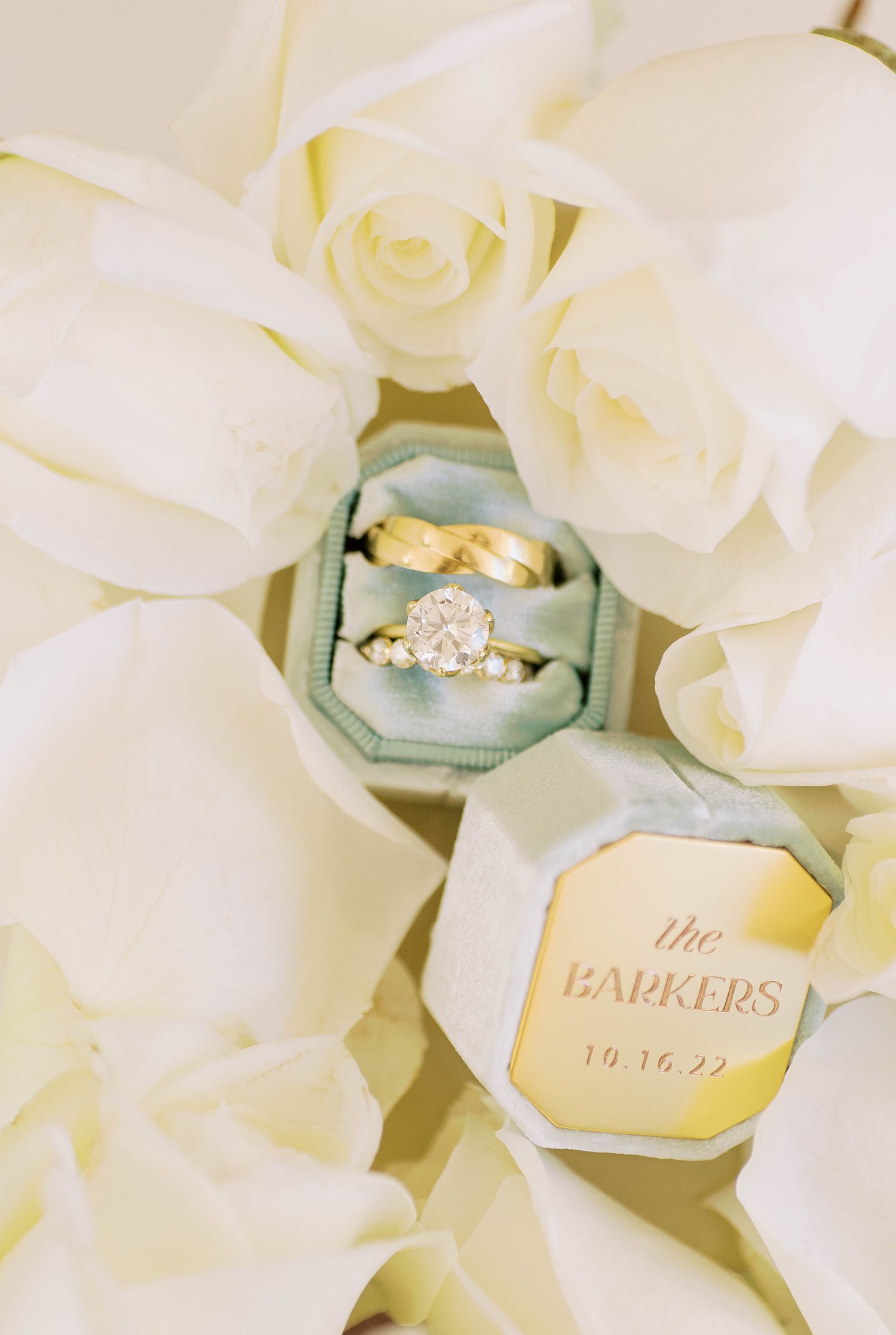 gold wedding bands rest in blue box among ivory roses