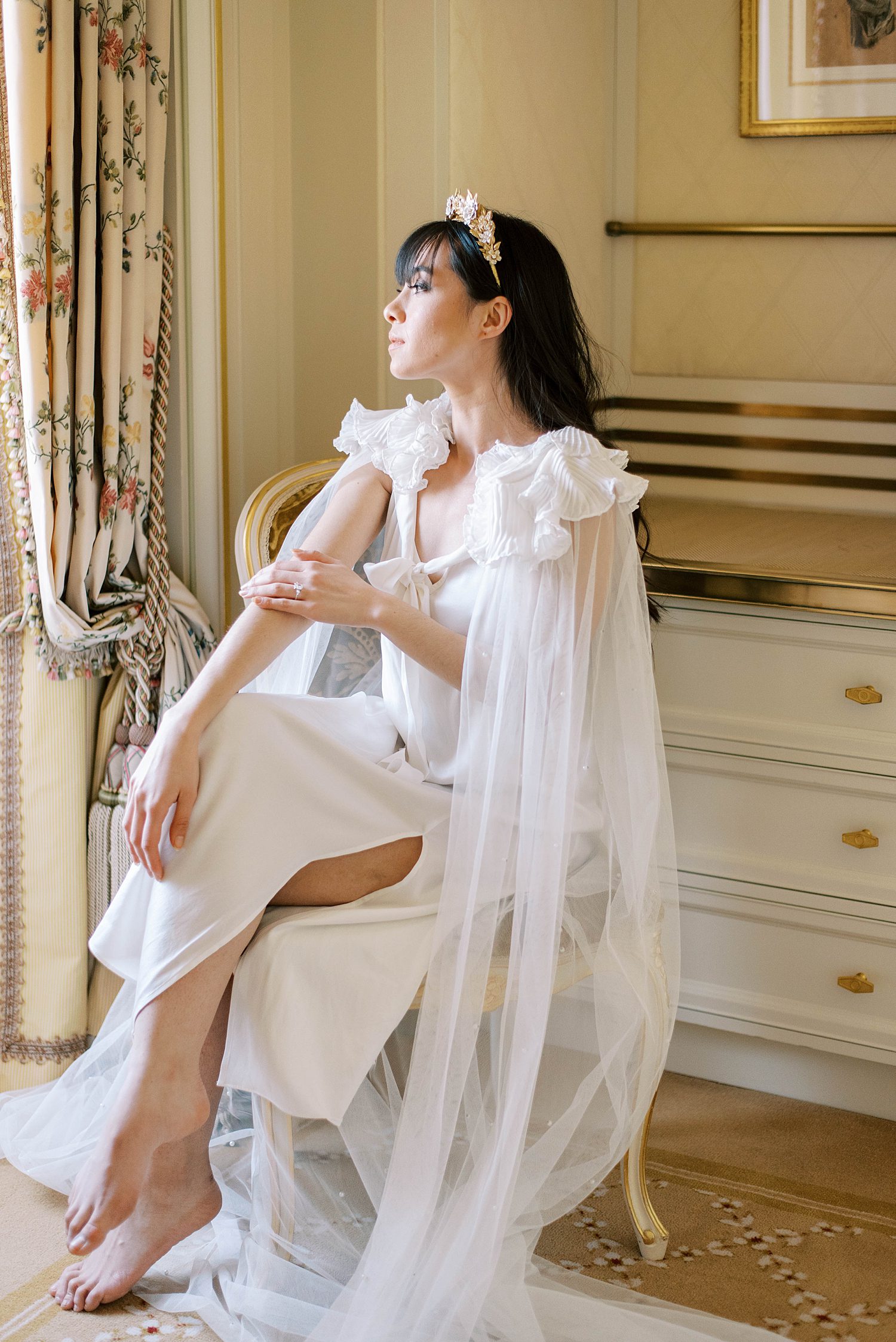 bride sits in elegant gown with gauze robe during Paris bridal boudoir session in Ritz