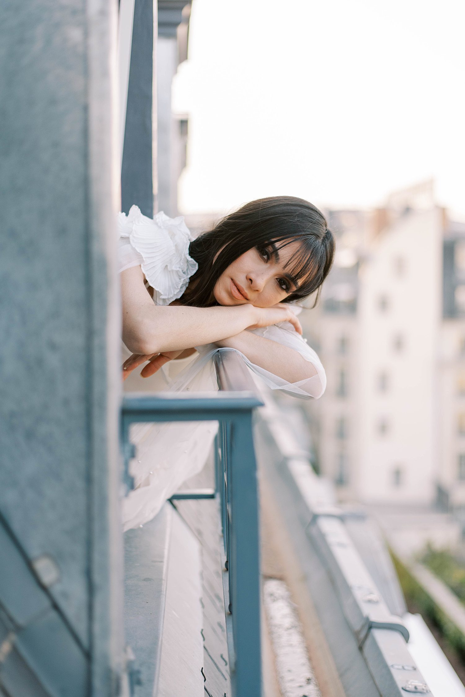 bride leans on blue balcony during portraits in Paris