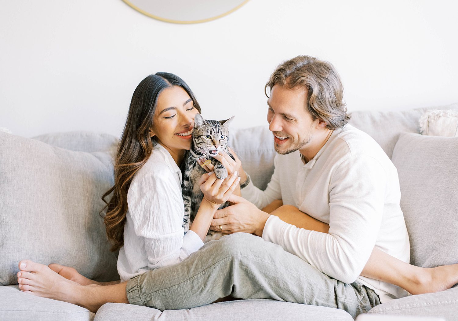 couple snuggles with cat sitting on couch during lifestyle anniversary portraits