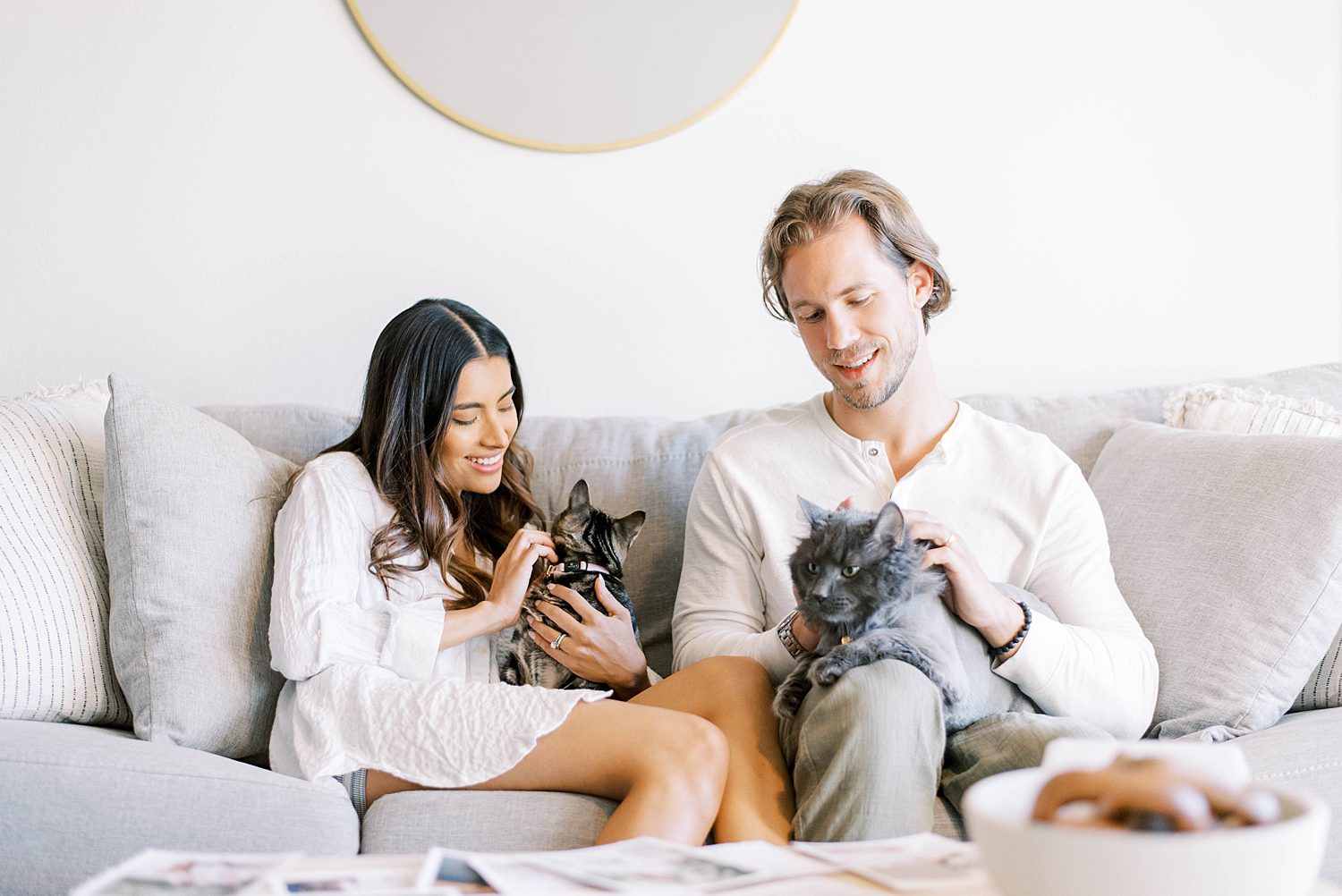 married couple sits on couch with two cats during lifestyle anniversary portraits