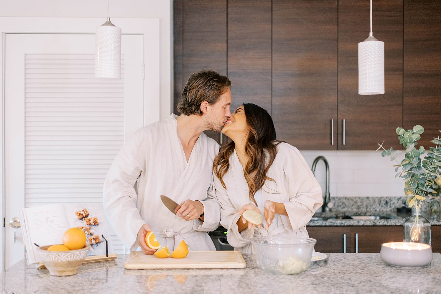 married couple kisses in kitchen while cooking during lifestyle anniversary portraits