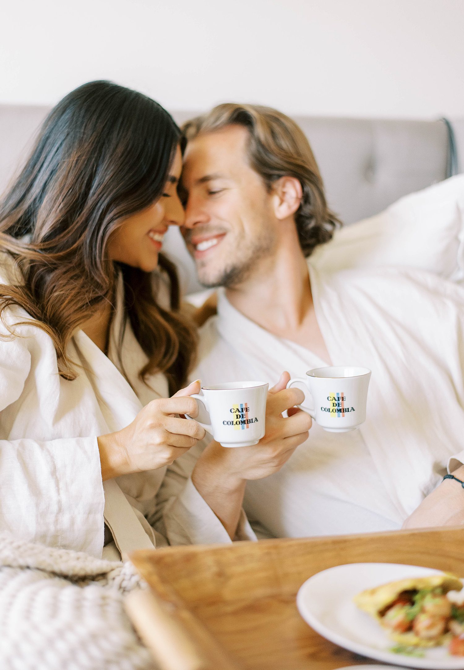 couple leans together with coffee cups in bed
