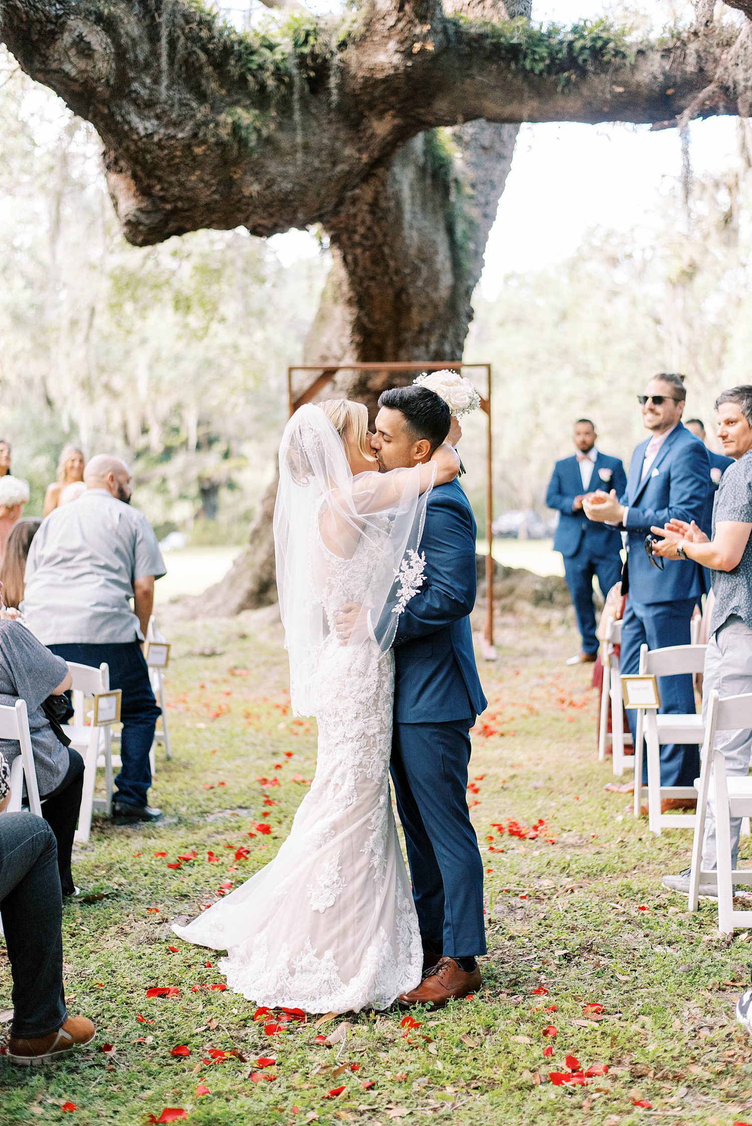 bride and groom kiss in aisle under tree at Philippe Park