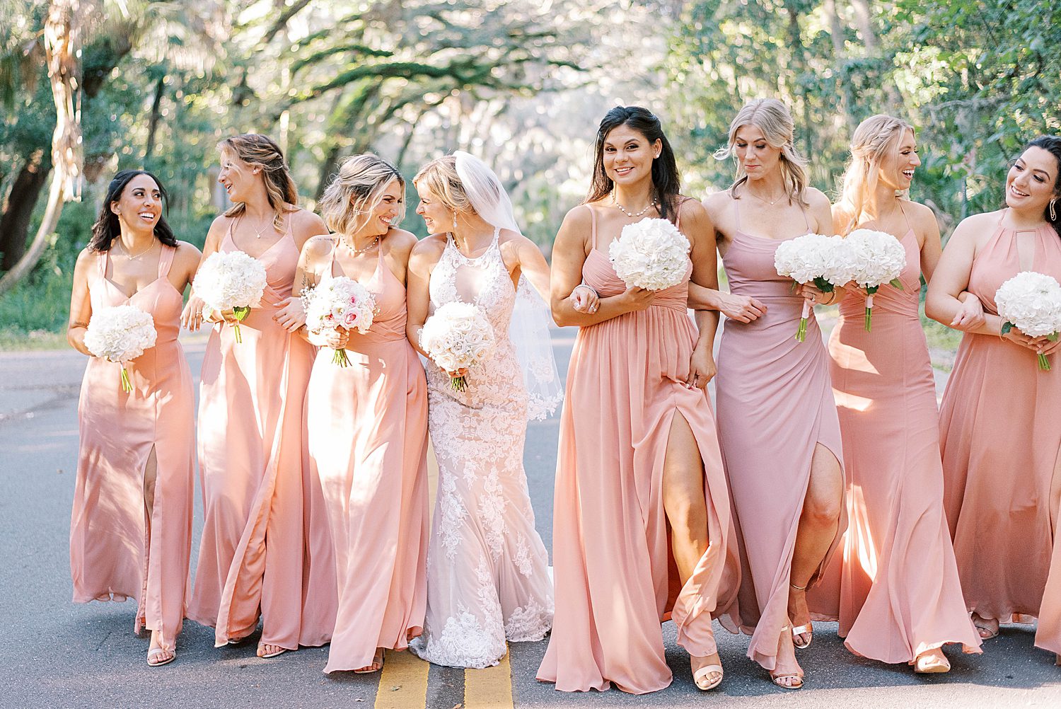 bride walks with bridesmaids in pink gowns at Philippe Park