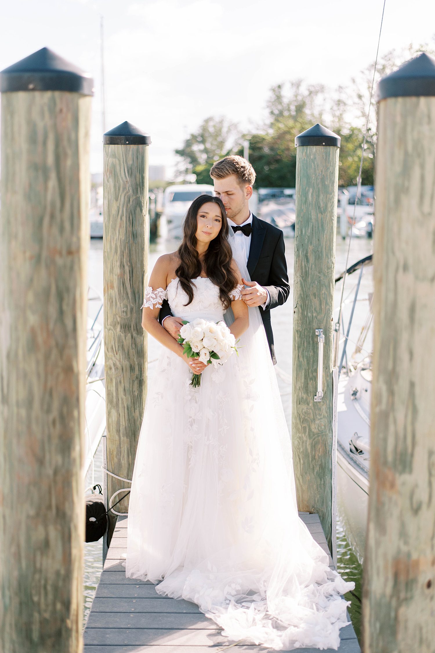bride and groom hug standing between wooden pillars on dock