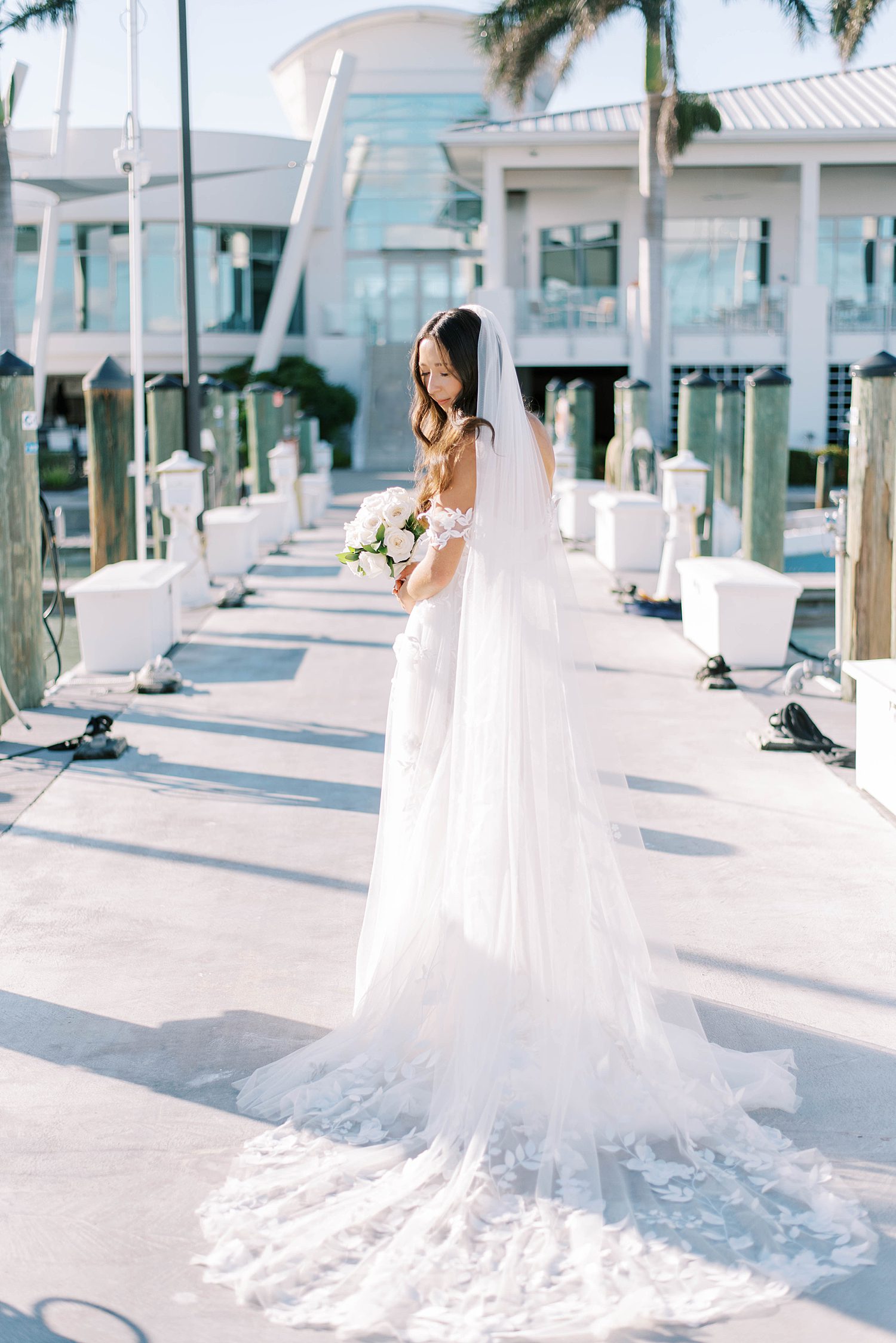 bride looks over shoulder in off-the-shoulder gown with lace details with veil behind her