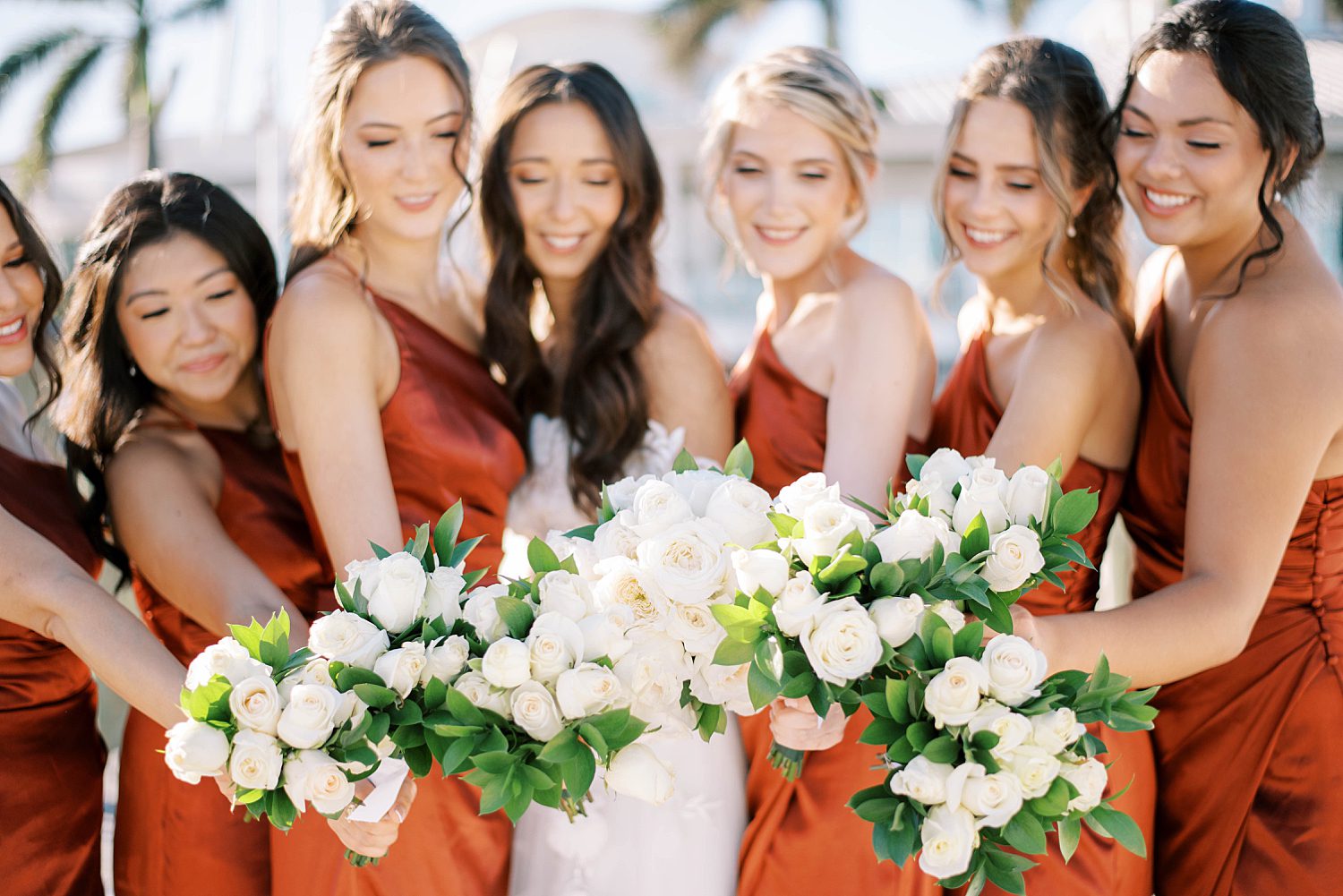 bride and bridesmaids hold out white bouquets in rust gowns