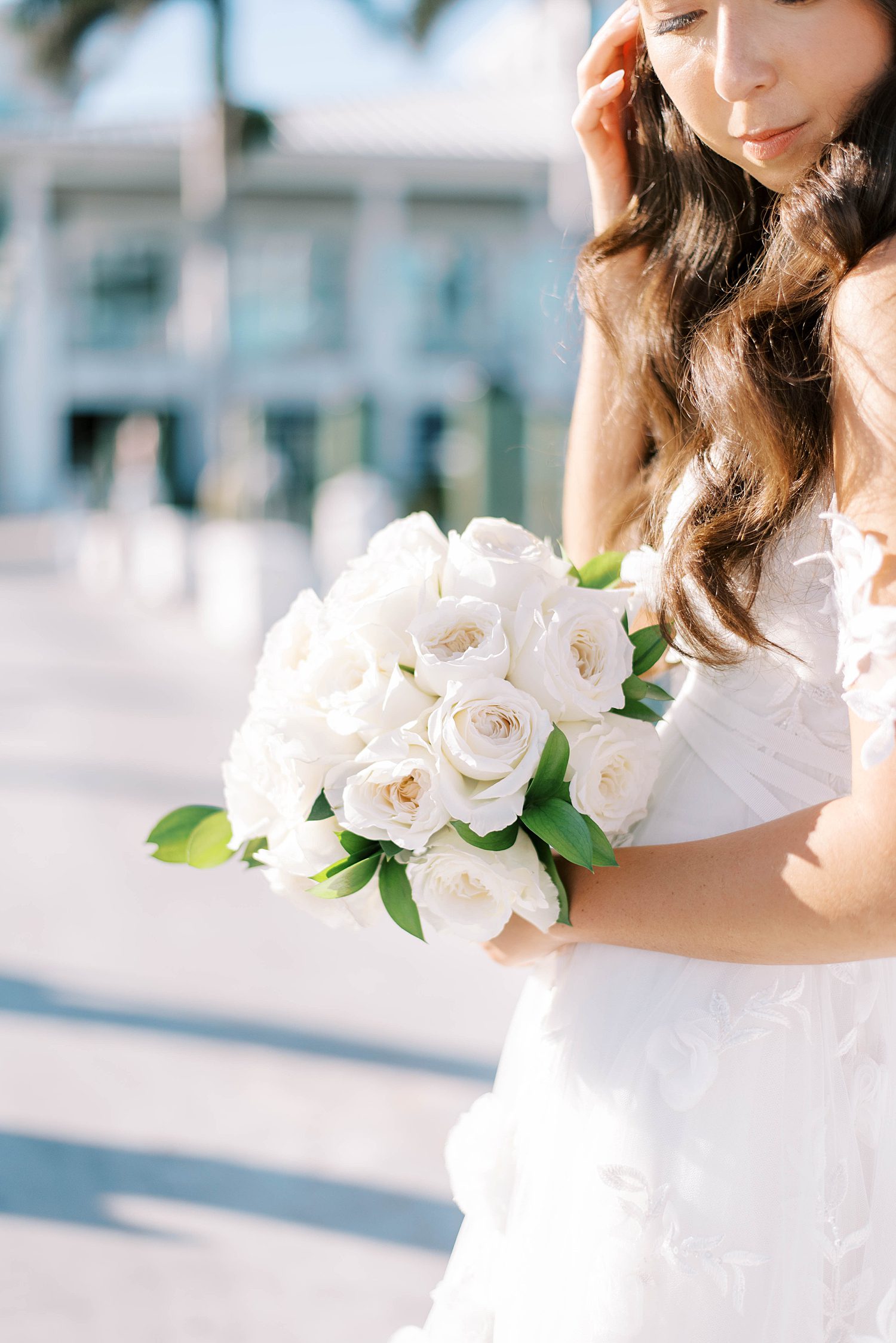 bride holds up all-white bouquet standing on dock at Sarasota Yacht Club