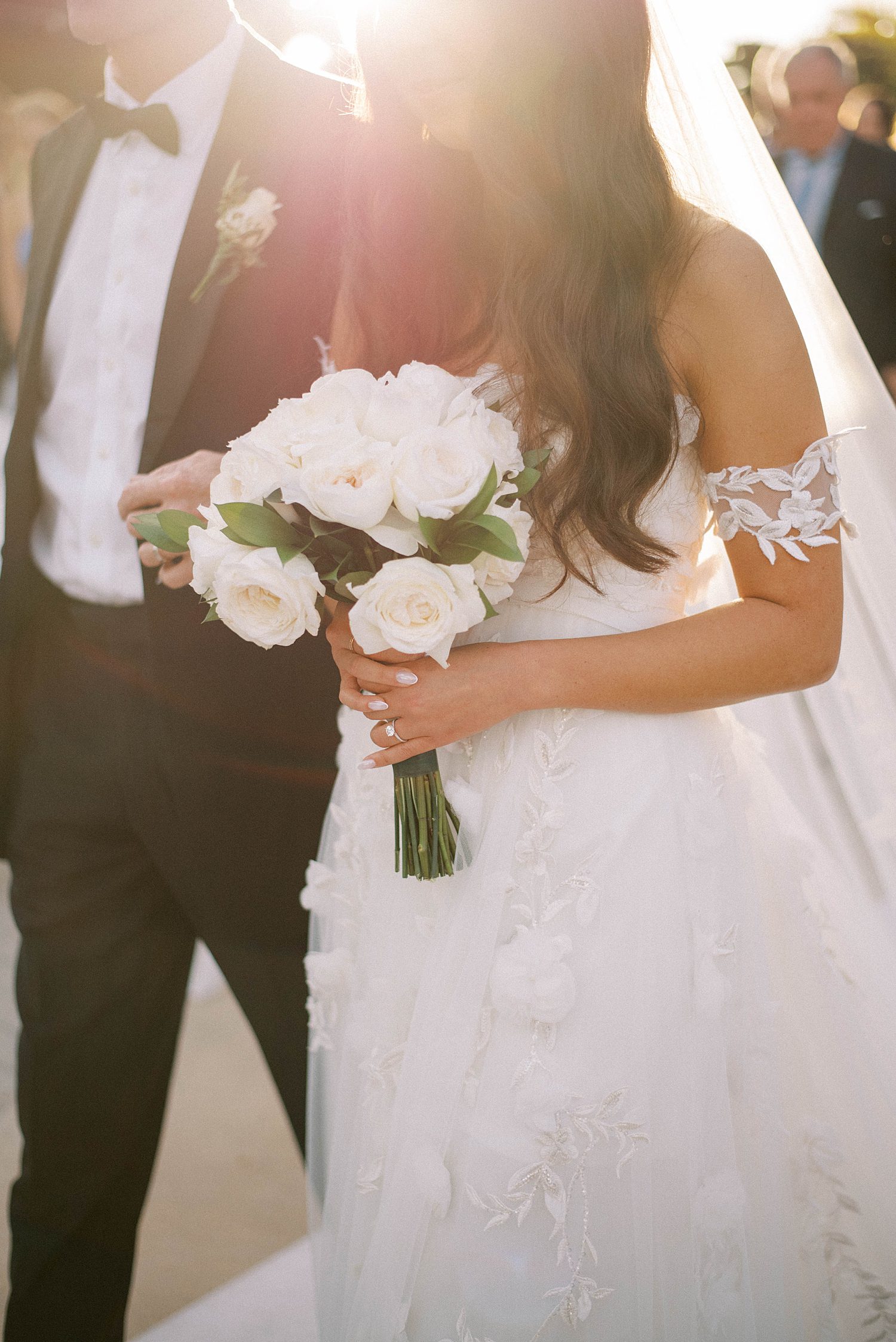 bride holds bouquet of white flowers walking down aisle