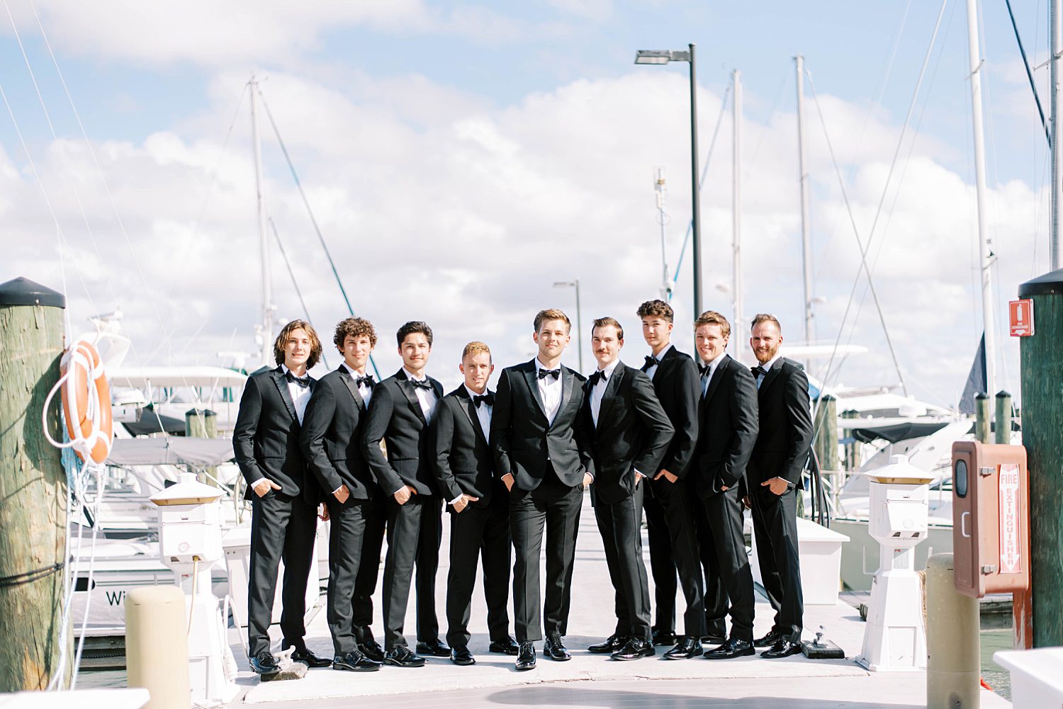 groom stands with groomsmen in classic black tucks on dock