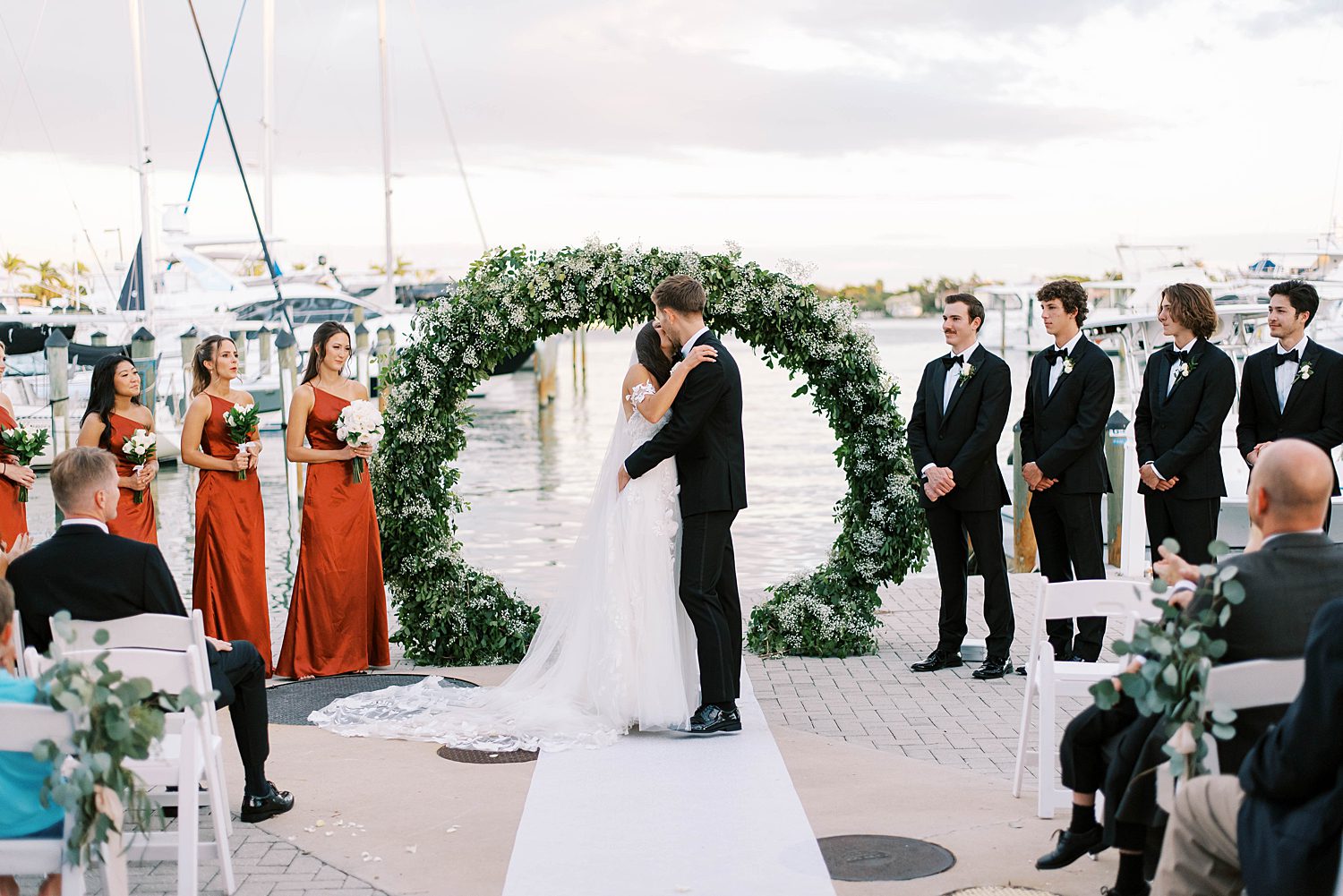 bride and groom kiss under green arbor at Sarasota Yacht Club