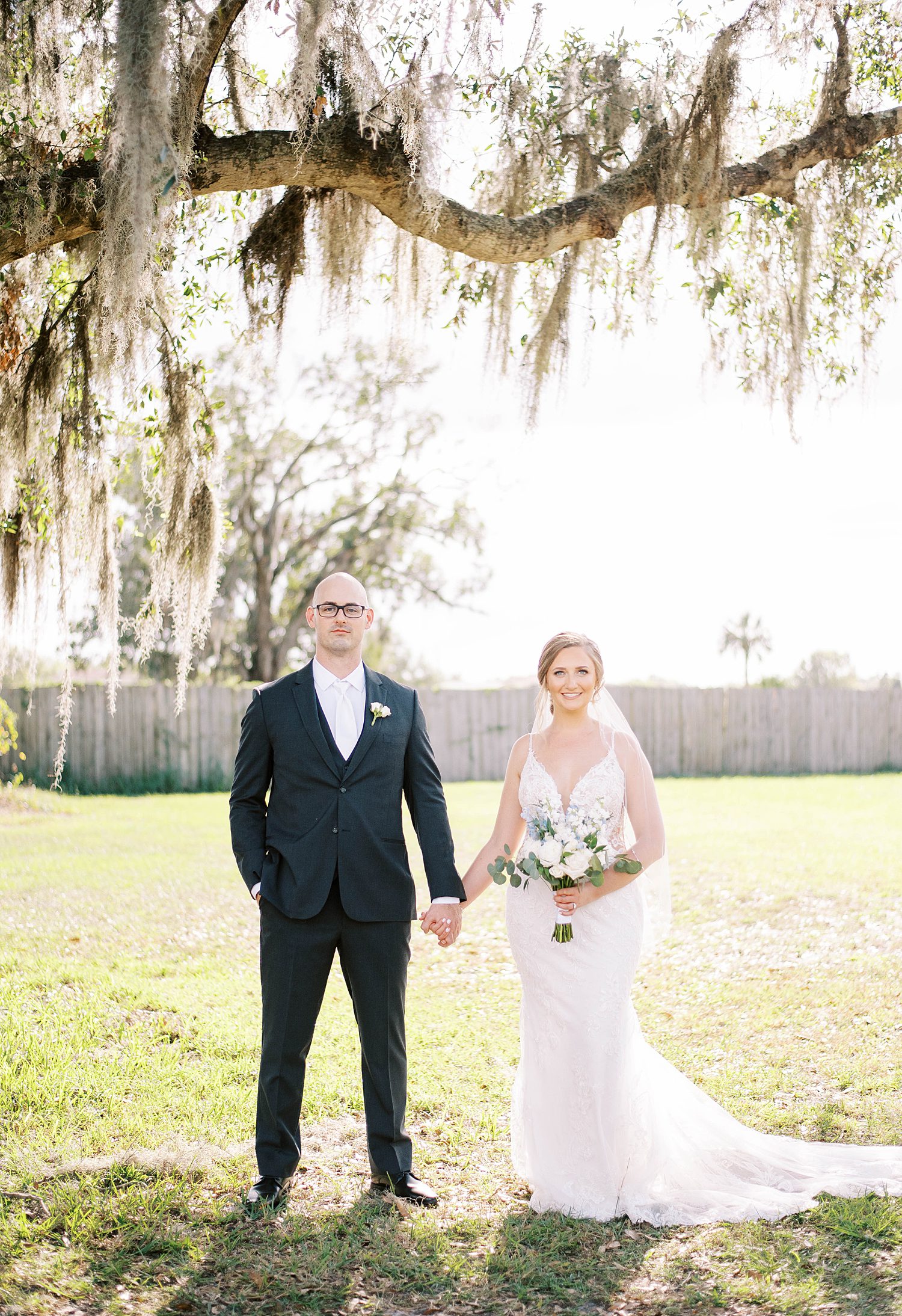 newlyweds hold hands standing under oak tree
