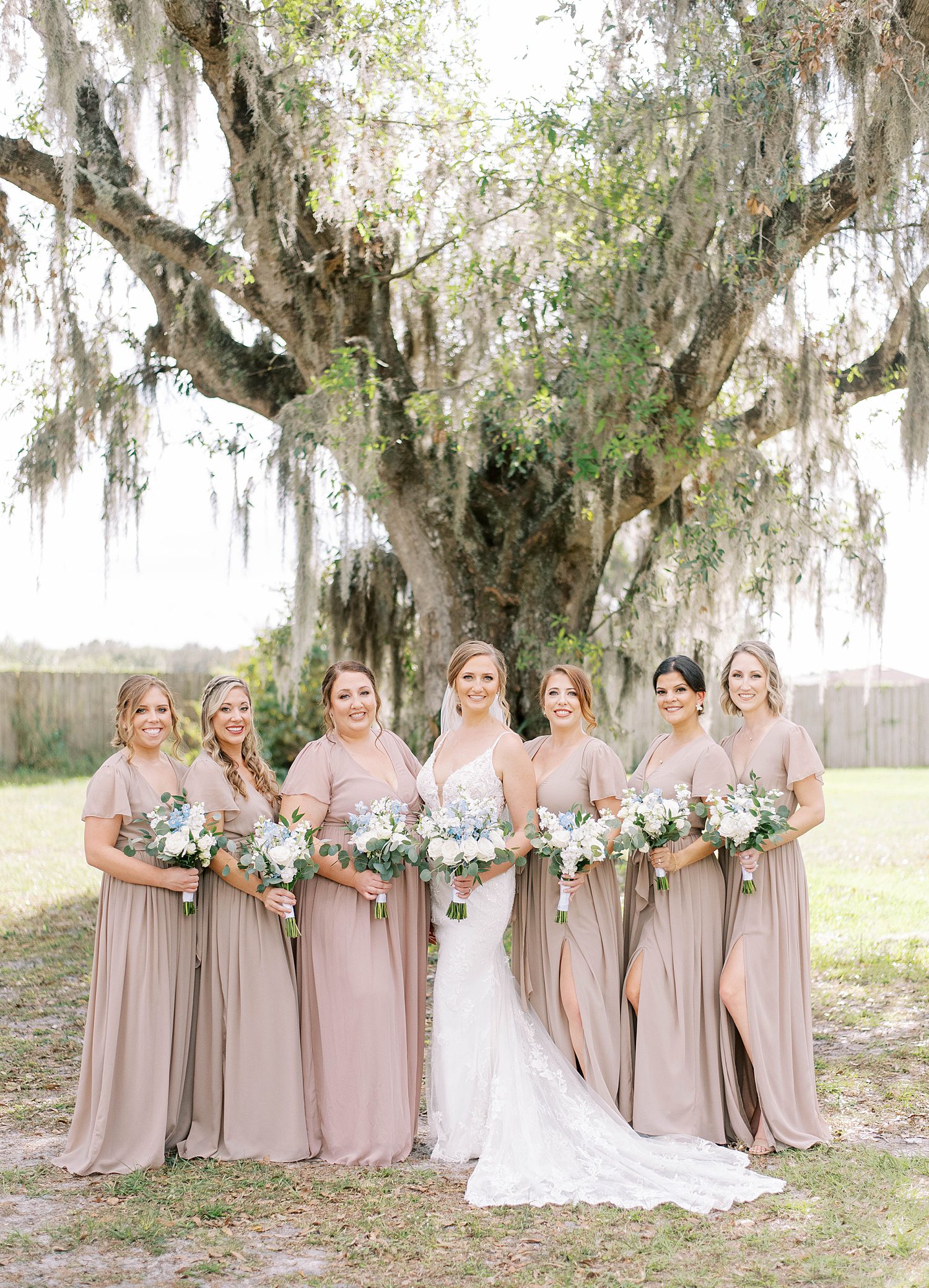 bride poses with bridesmaids under oak tree at The Barn at Lone Oak Acres