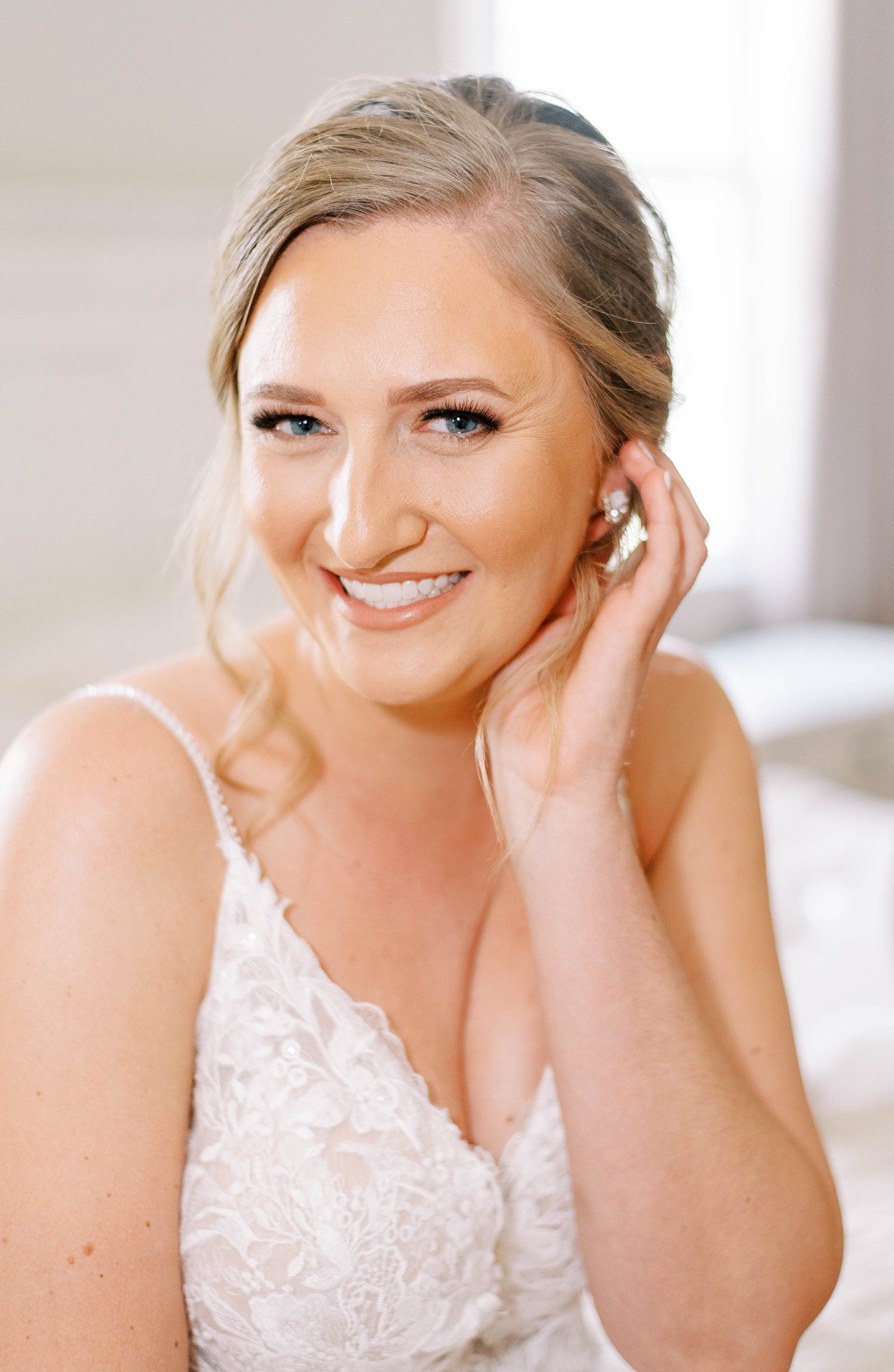 bride pushes hair behind her ear smiling in wedding dress
