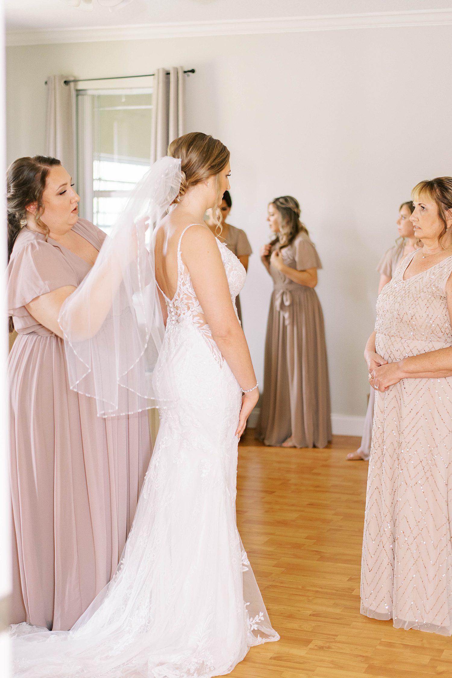 mother and bridesmaids help bride into wedding dress and veil