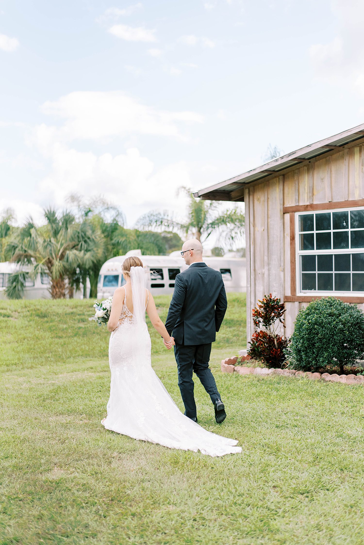 bride and groom hold hands walking by barn at The Barn at Lone Oak Acres