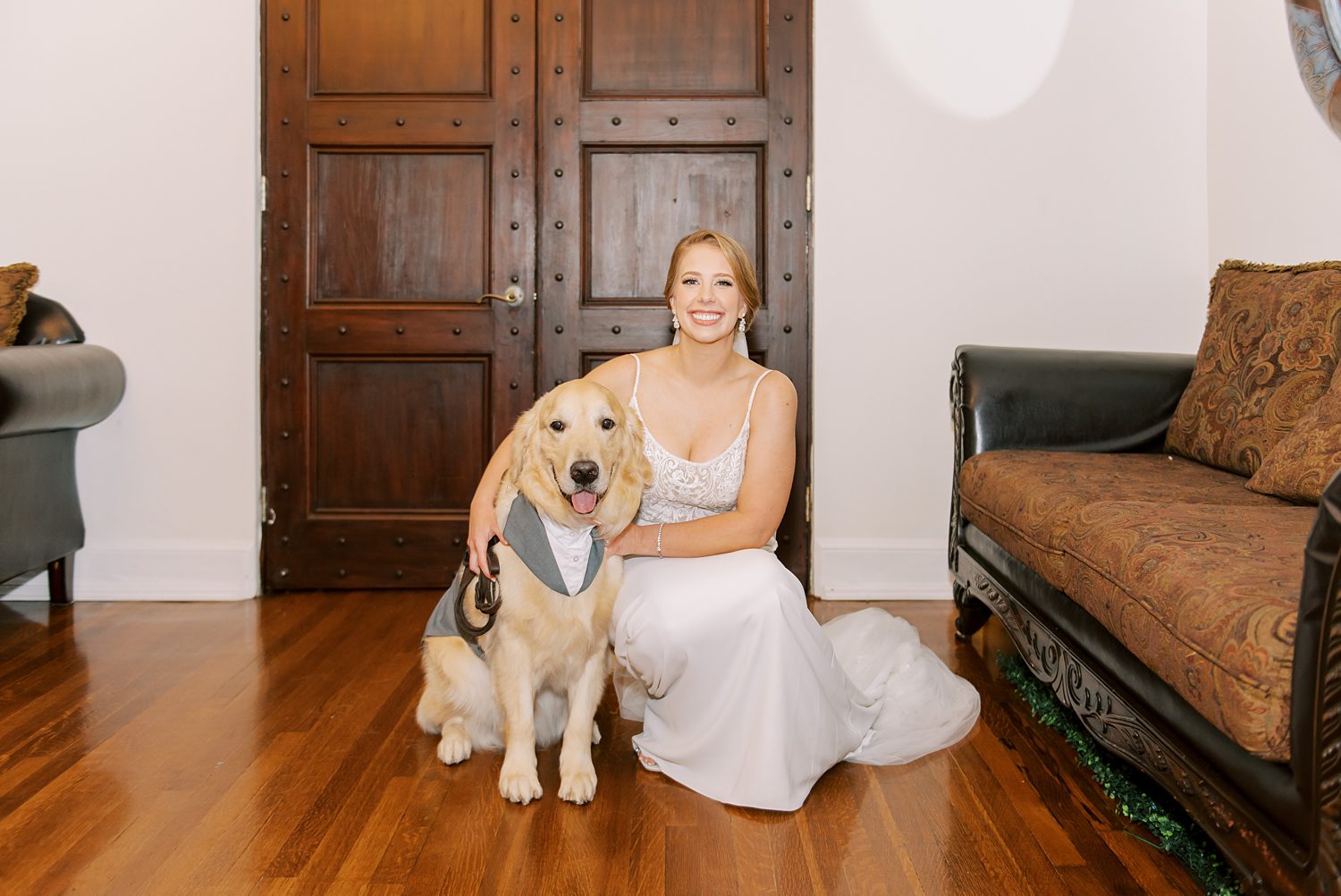 bride kneels beside dog in tuxedo