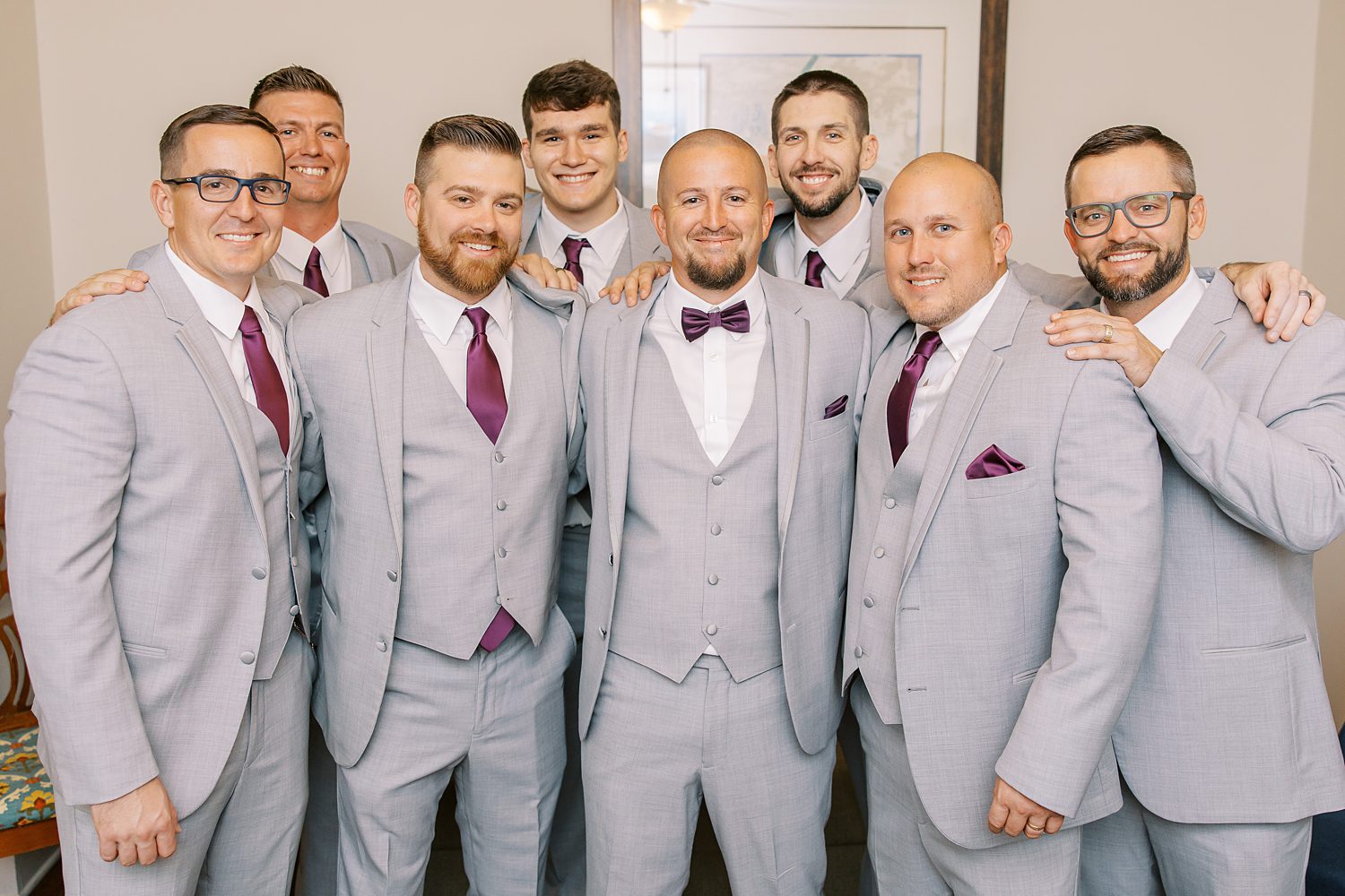 groom poses with groomsmen in grey suits with plum ties