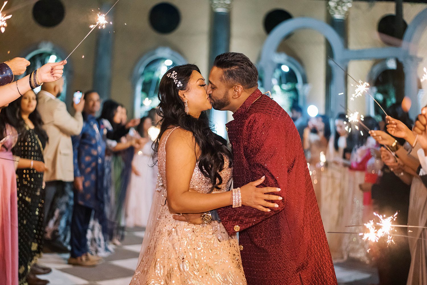 newlyweds kiss in traditional Indian attire leaving sparkler exit