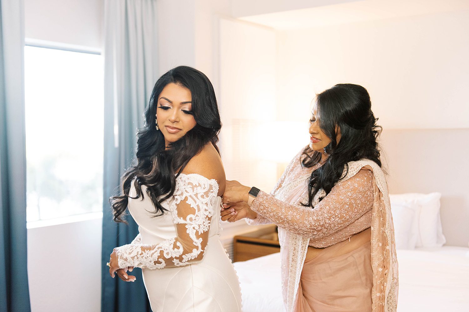 mother helps bride into lace wedding gown