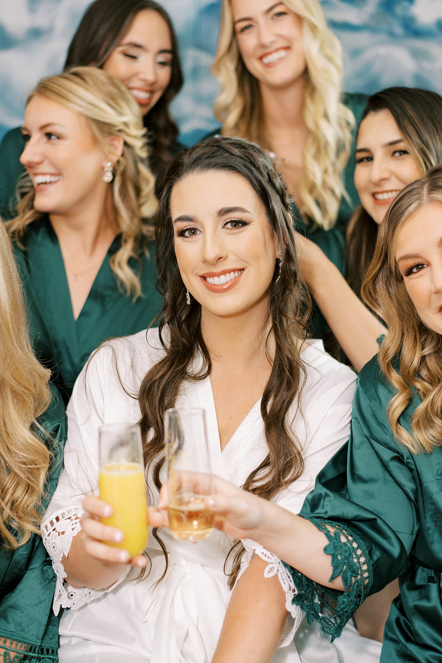 bride poses with bridesmaids in emerald robes toasting mimosas 