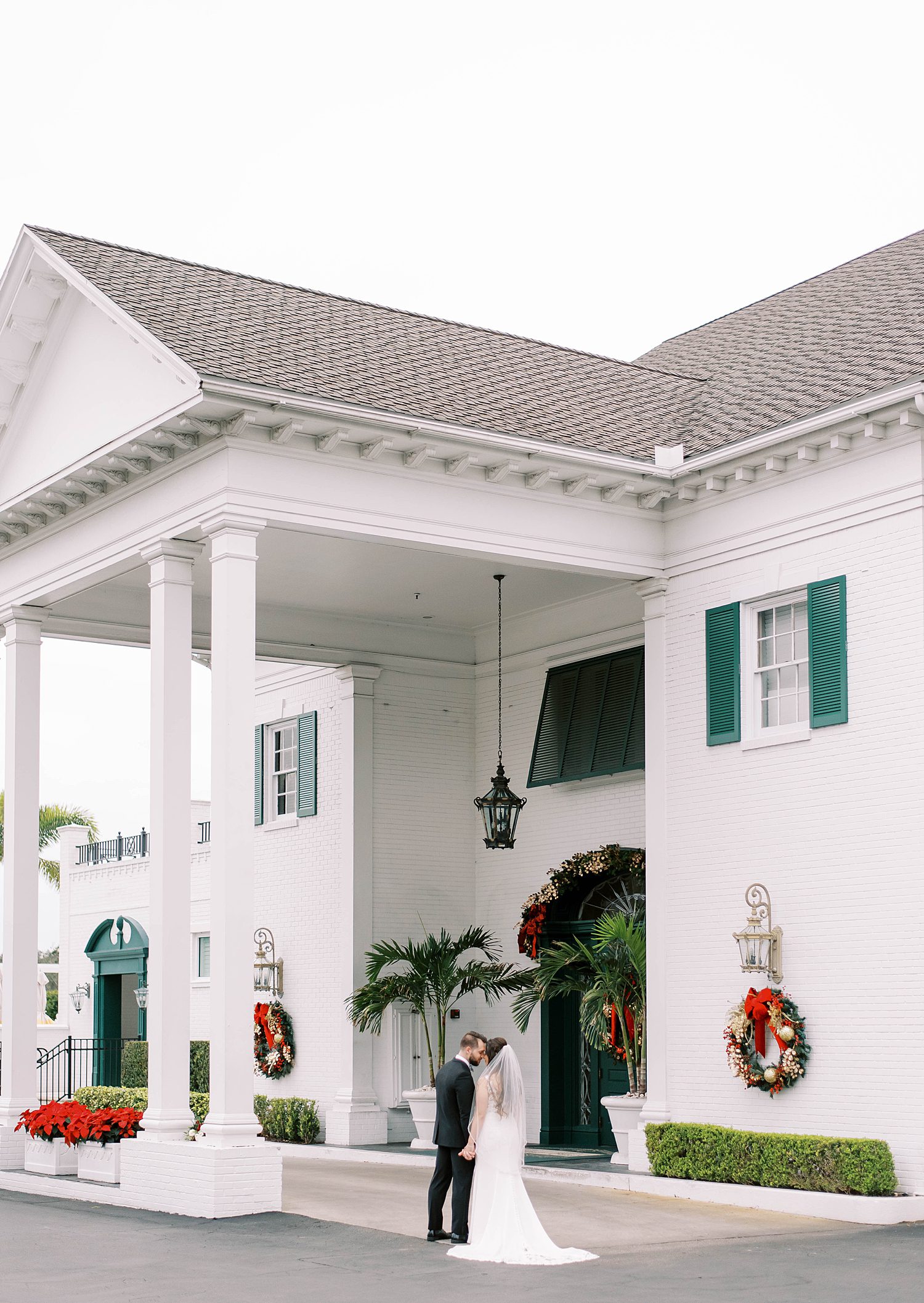 bride and groom pose outside Palma Ceia Country Club with Christmas decorations 