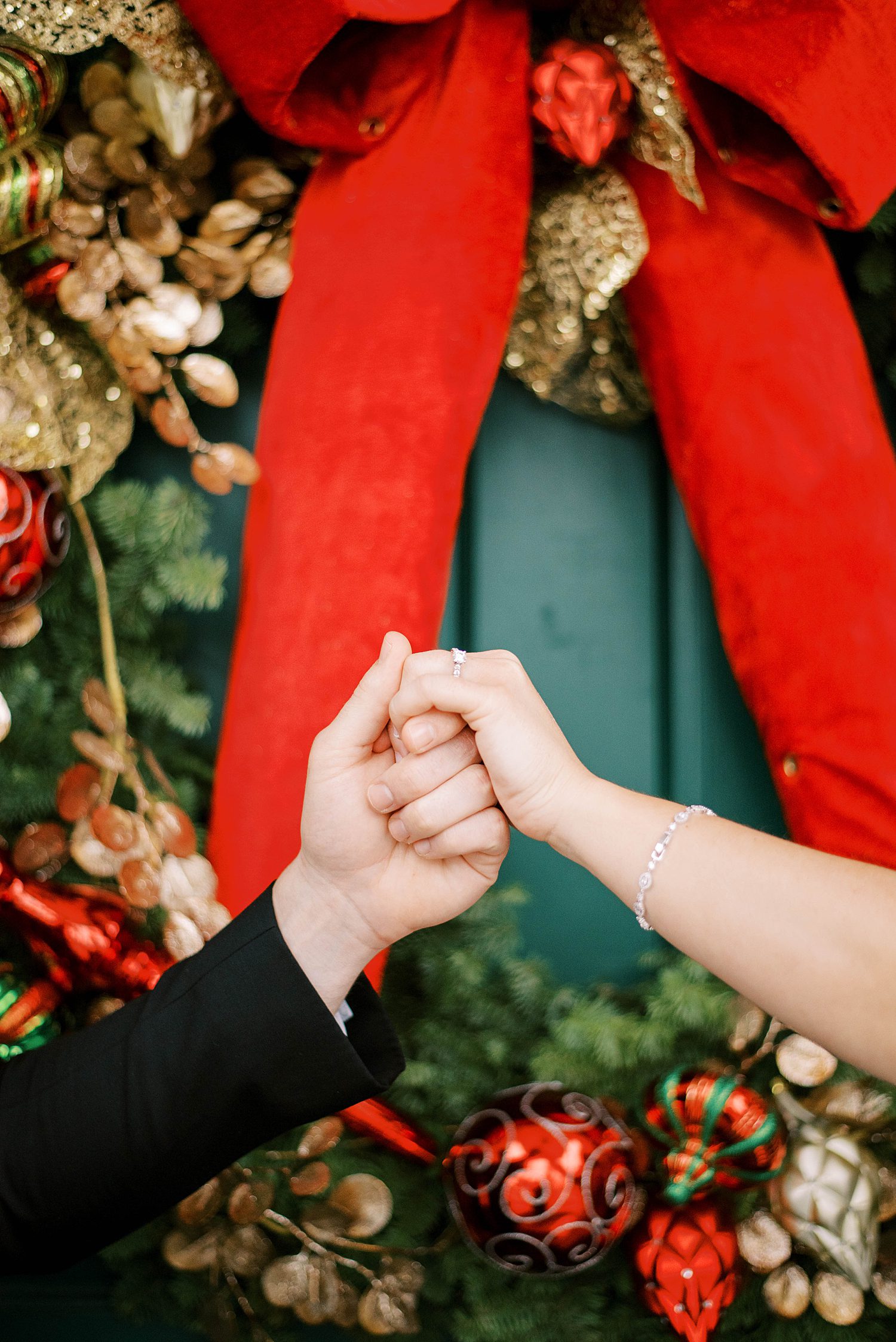 groom holds bride's hand in front of door with Christmas wreath 