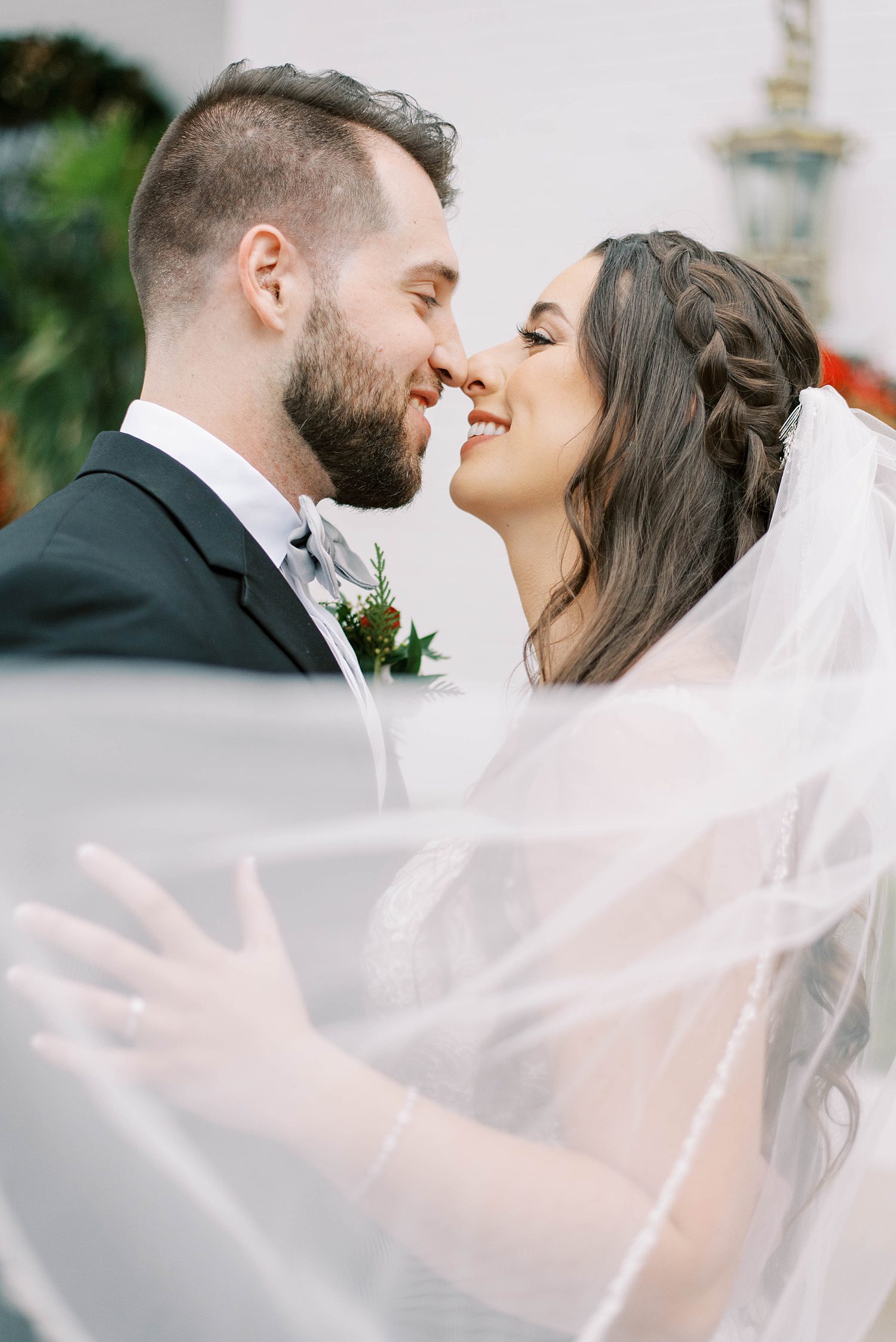 bride and groom nuzzle noses with veil around them 