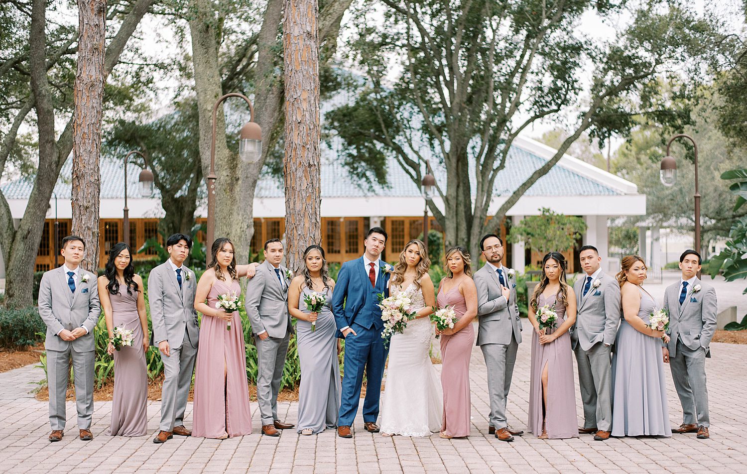 bride and groom pose with wedding party in mismatched blue and purple gowns and grey suits 